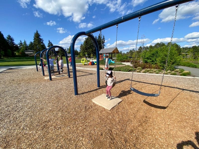 Toddler girl smiling on the swings at Surrey Downs Park in Bellevue, enjoying this peaceful and family-friendly playground surrounded by trees and open green space.