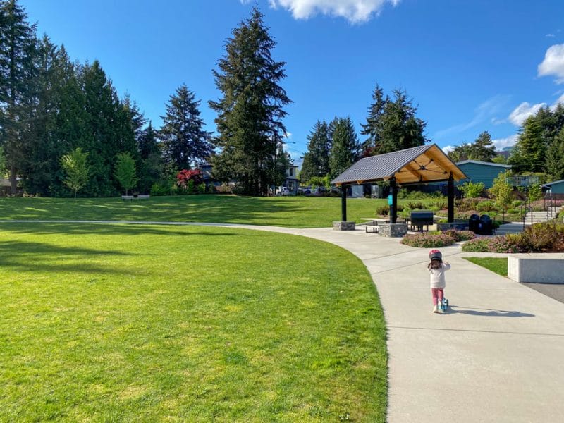 Young girl riding her scooter around the paved loop at Surrey Downs Park in Bellevue, a popular family-friendly park with wide paths, open green space, and a modern playground.