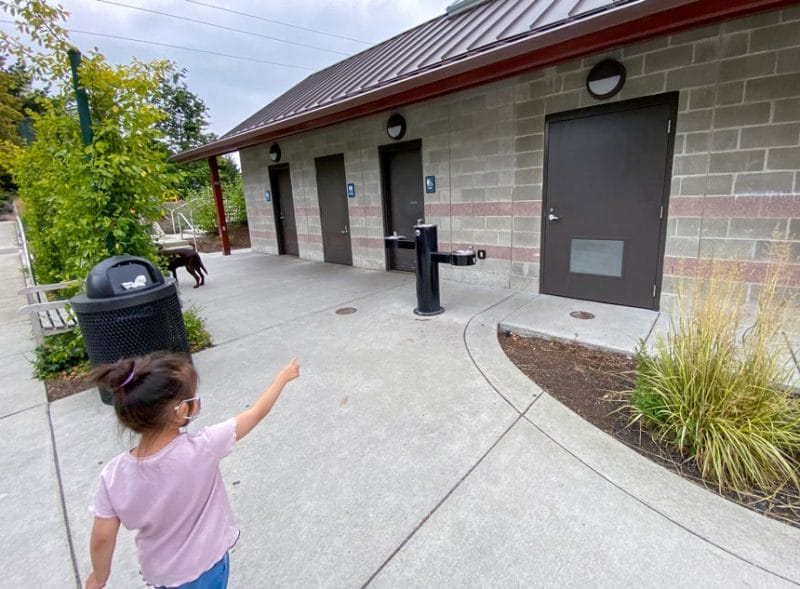 Bellevue Downtown Park features clean and convenient family-friendly restrooms right next to the playground. In this photo, a young girl excitedly points to the family bathroom door—perfect for parents with toddlers or multiple kids.