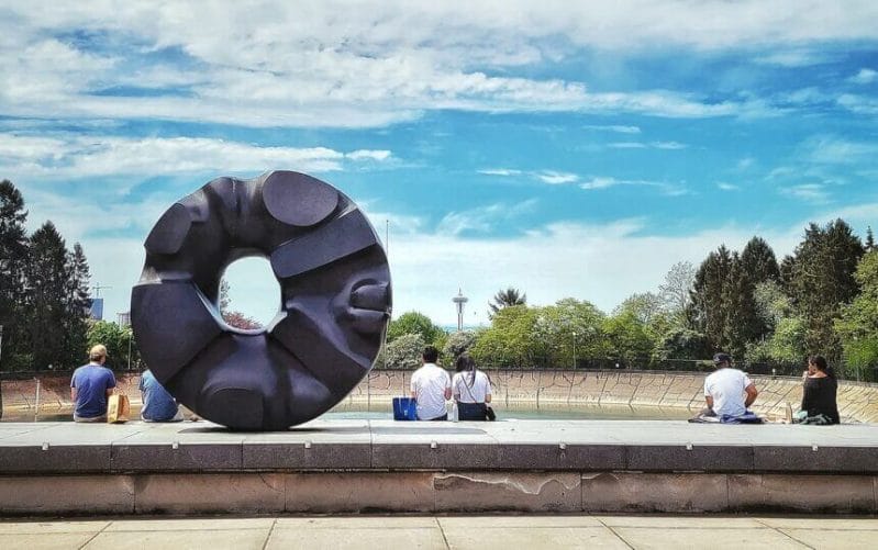 Large black art sculpture at Volunteer Park in Seattle, with a perfect circular opening that frames the iconic Space Needle in the background. This popular photo spot is part of a family-friendly visit to Volunteer Park, where kids can run around, explore nature, and enjoy cultural attractions nearby like the Seattle Asian Art Museum—making it a great stop on a Seattle family itinerary.