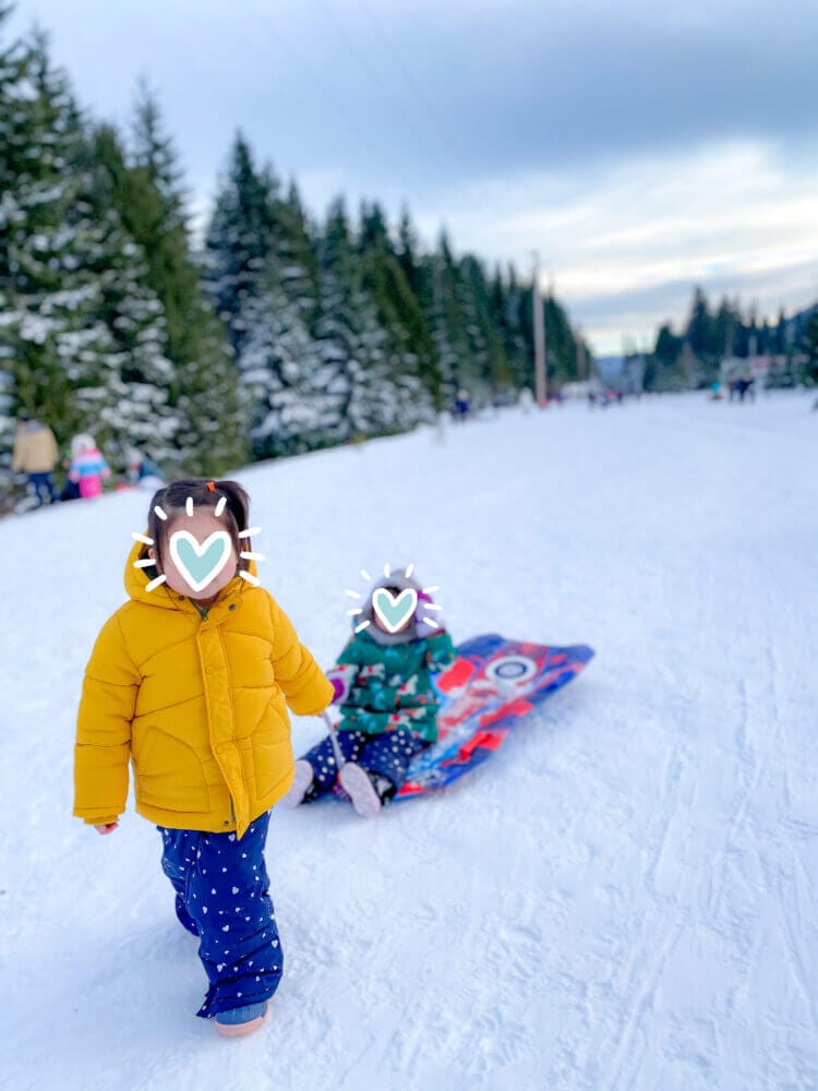 Young toddler girl pulling her friend on a sled through the snow at Hyak Sno-Park, a popular family-friendly winter destination near Seattle known for its scenic sledding hills and snowy fun.