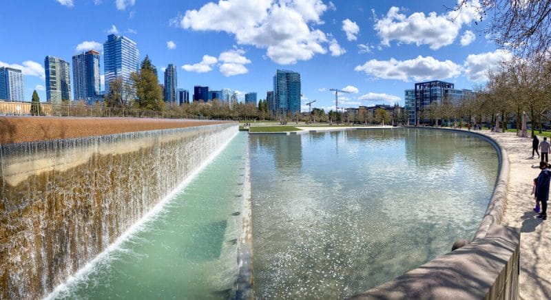 Cascading waterfall at Bellevue Downtown Park, flowing into a shallow reflecting pond surrounded by wide open lawns and paved walkways. This scenic feature is a highlight for families visiting one of the best parks for kids on the Eastside, offering space to play, scooter, and relax just steps from downtown Bellevue.