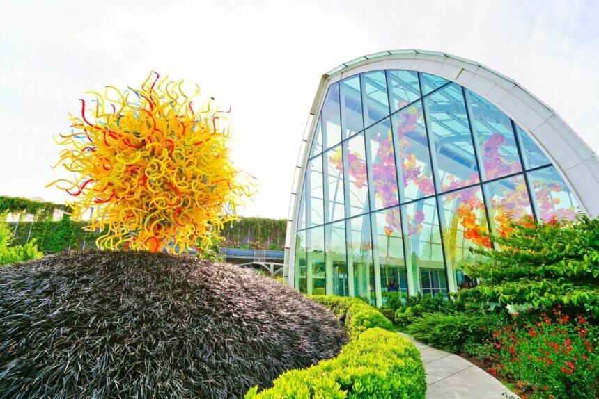 View of Chihuly Garden and Glass from the outside walk way looking at the hall of glass where a huge glass sculpture is hanging in a glass building