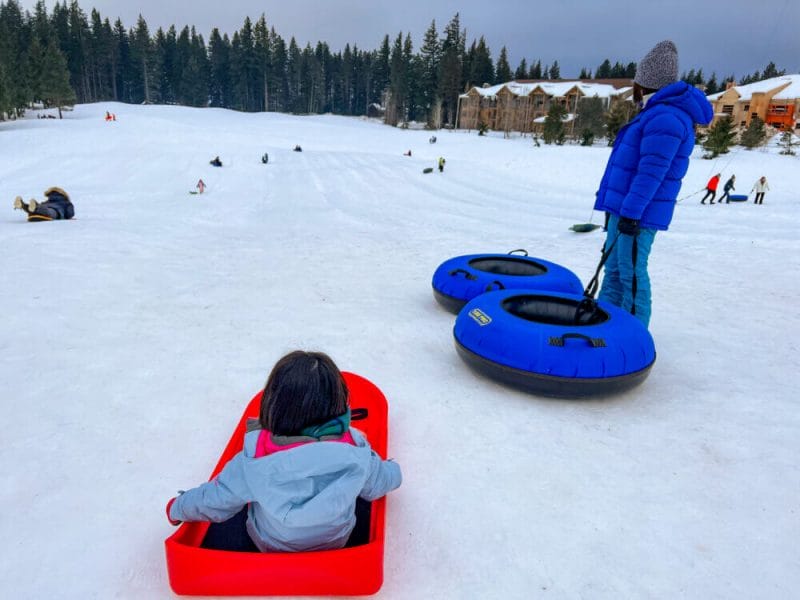 Mom and daughter at the Suncadia tubing hill, with the girl in a sled and mom holding a tube from Suncadia Resort during winter.