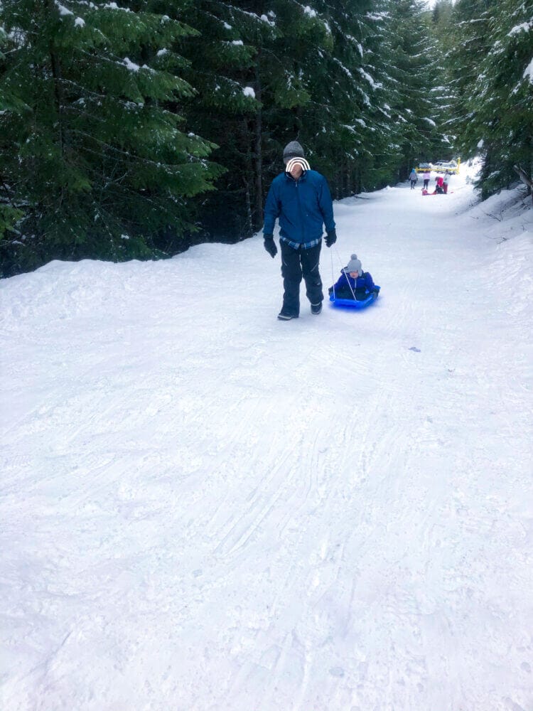 Dad pulling his child up the snowy slope at the Half Camp unofficial sledding hill near Snoqualmie Pass, a lesser-known but beloved local spot for families looking for free winter fun. With open hillsides perfect for sledding, this informal area is a great option for parents seeking a quieter, low-key snow play destination that’s still packed with excitement for kids.