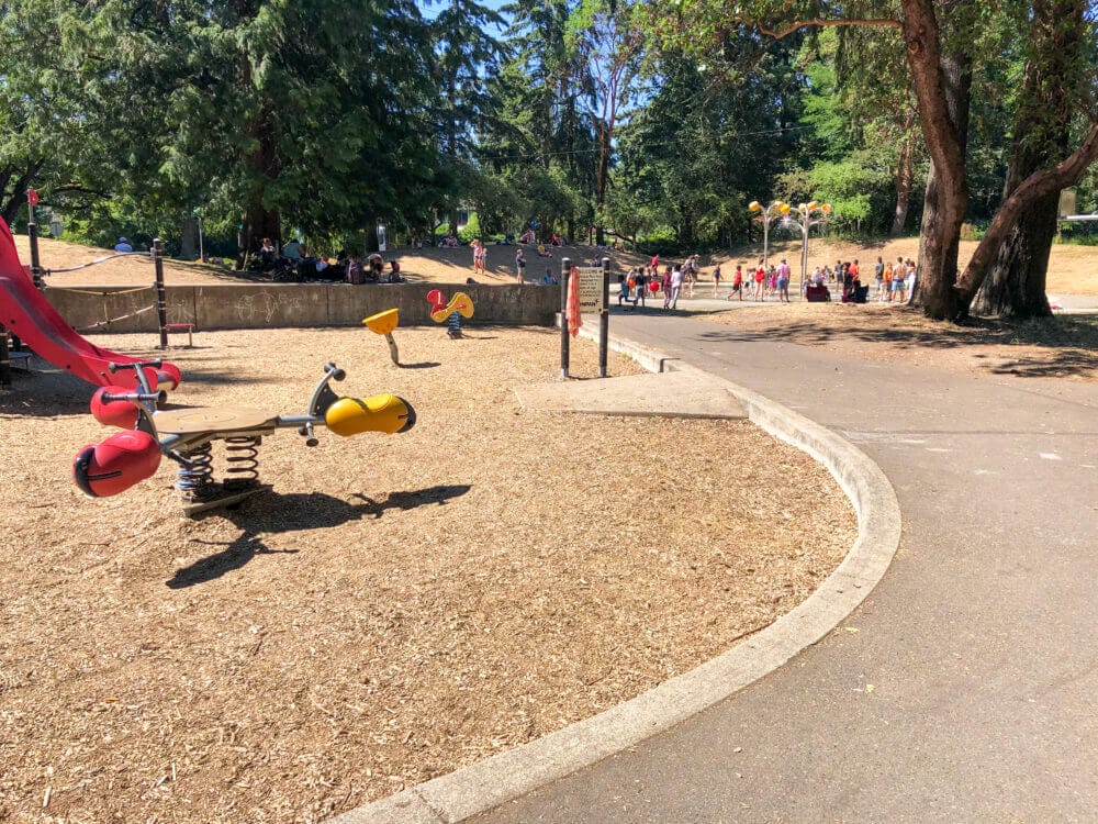 Kids playing and cooling off at the Northacres Park Spraypark in Seattle, with colorful water features and sprays in the background on a sunny summer day.