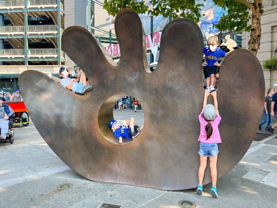 Mariners Baseball game Seattle, Kids taking photo in front of the stadium on the large metal baseball glove art sculpture.