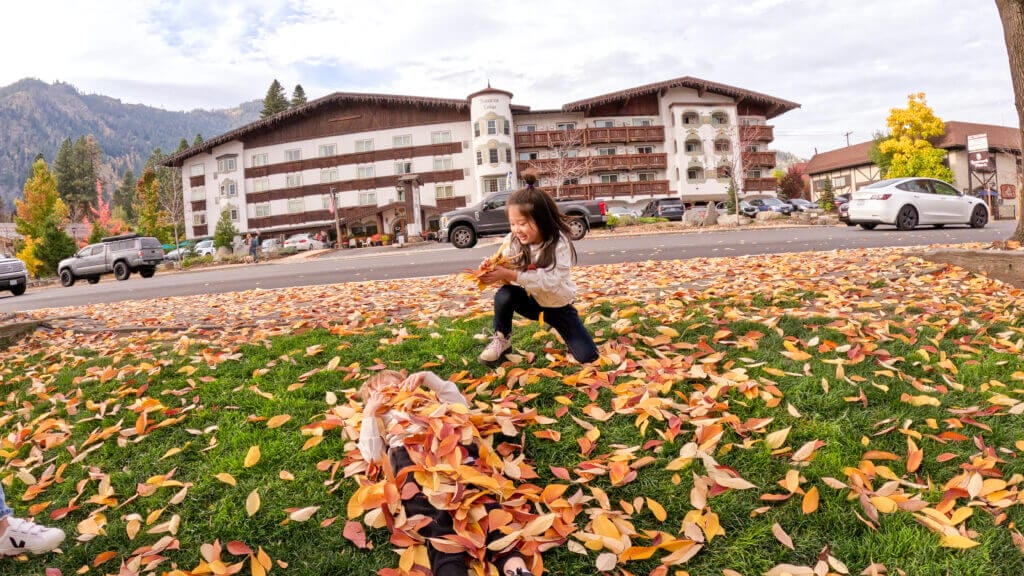 Kids playing in fall-colored leaves in front of the Bavarian Lodge in Leavenworth, Washington, with the hotel’s charming Bavarian-style architecture in the background.