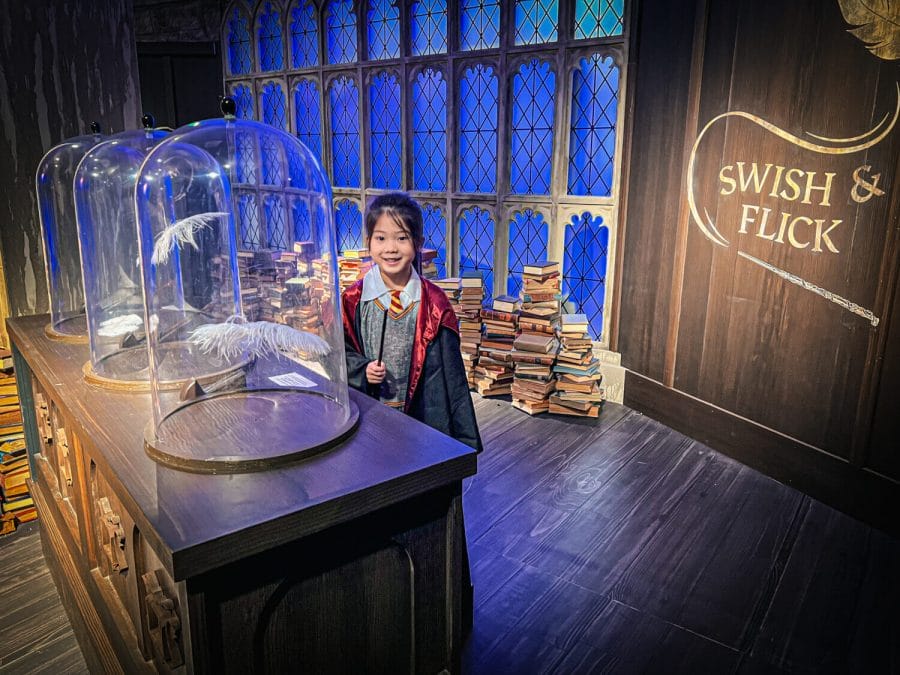 Harry Potter Magic at Play Seattle Bellevue Girl posing with her wand at the interactive Swish and Flick exhibit where a feather will slowly raise up in a glass container