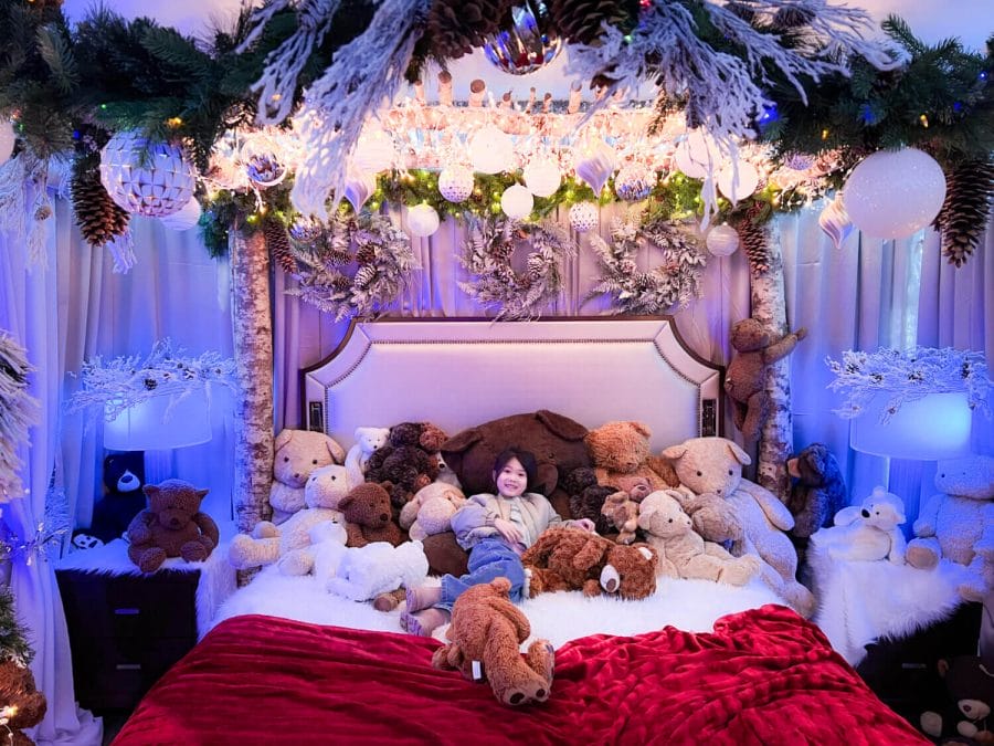 The Fairmont Olympic Hotel's Teddy Bear Suite, a girl lying down in the queen bed with more than 20 teddy bears with holiday lights above and to the side.
