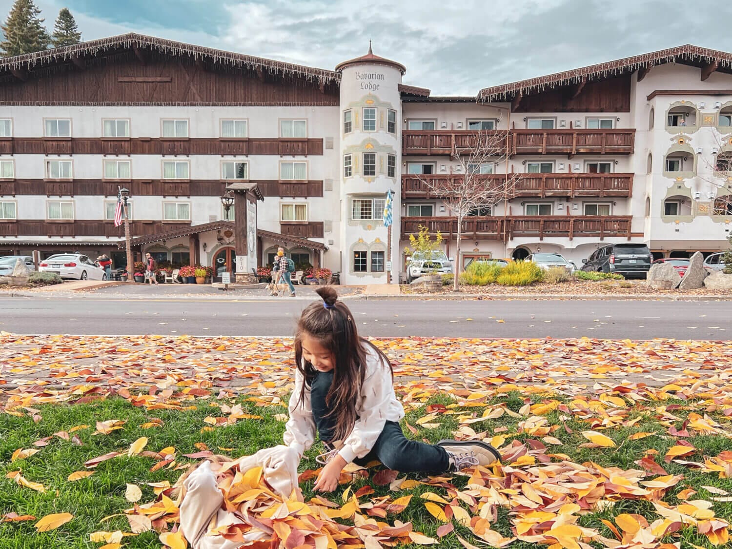 Kids playing in fall-colored leaves in front of the Bavarian Lodge in Leavenworth, Washington, with the hotel’s charming Bavarian-style architecture in the background.