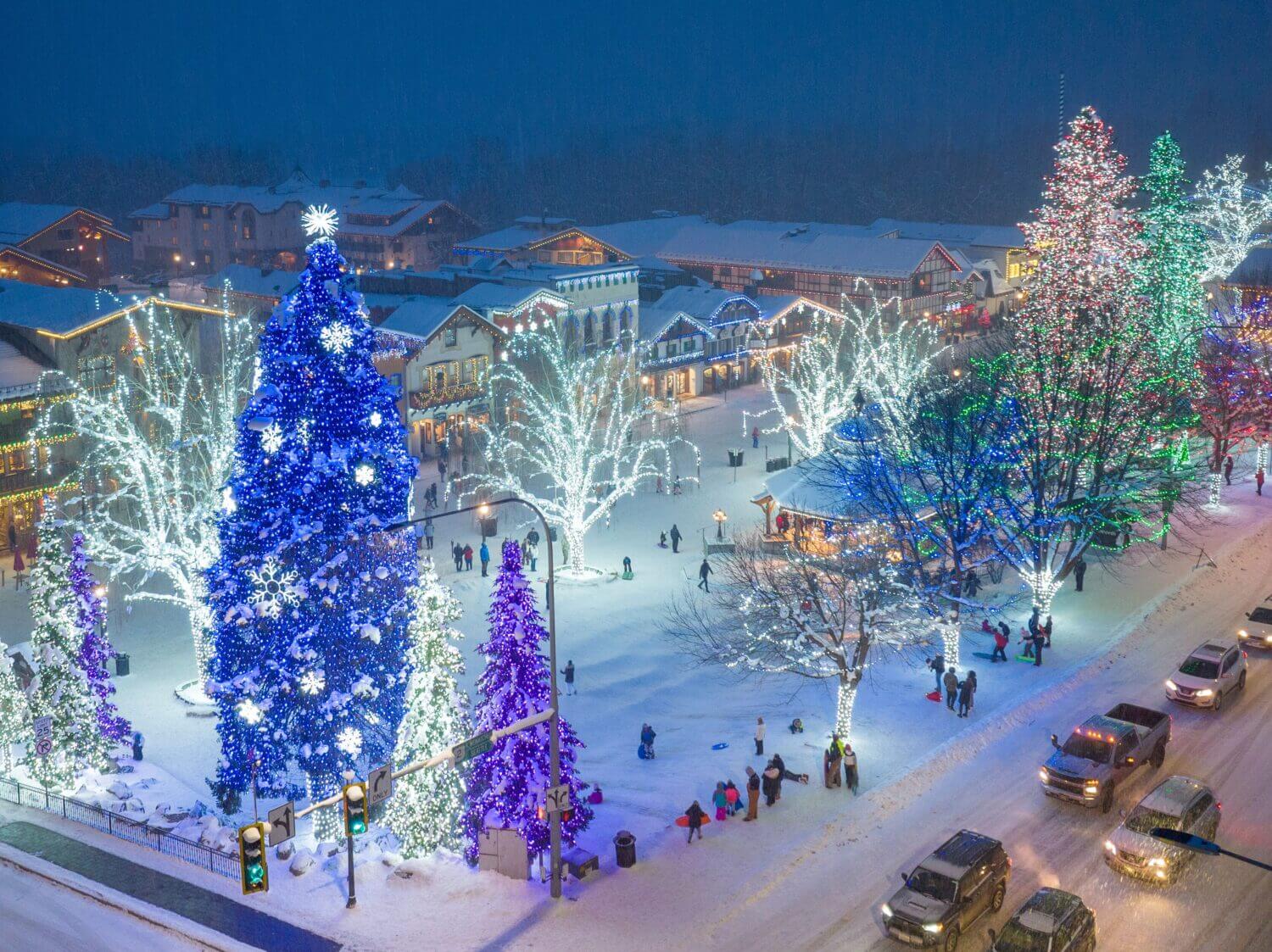 Aerial shot of snowy Leavenworth town center adorned with holiday lights, showcasing Bavarian-style buildings and festive decorations.