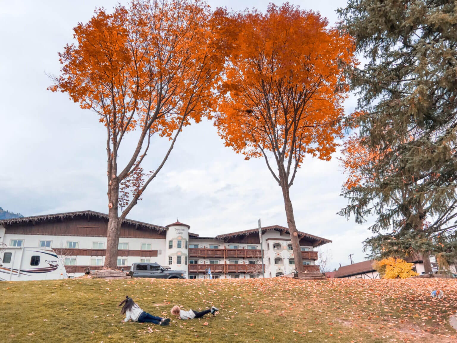 Kids rolling down a hill covered in fall-colored leaves at Front Street Park in Leavenworth, with vibrant autumn foliage in the background.