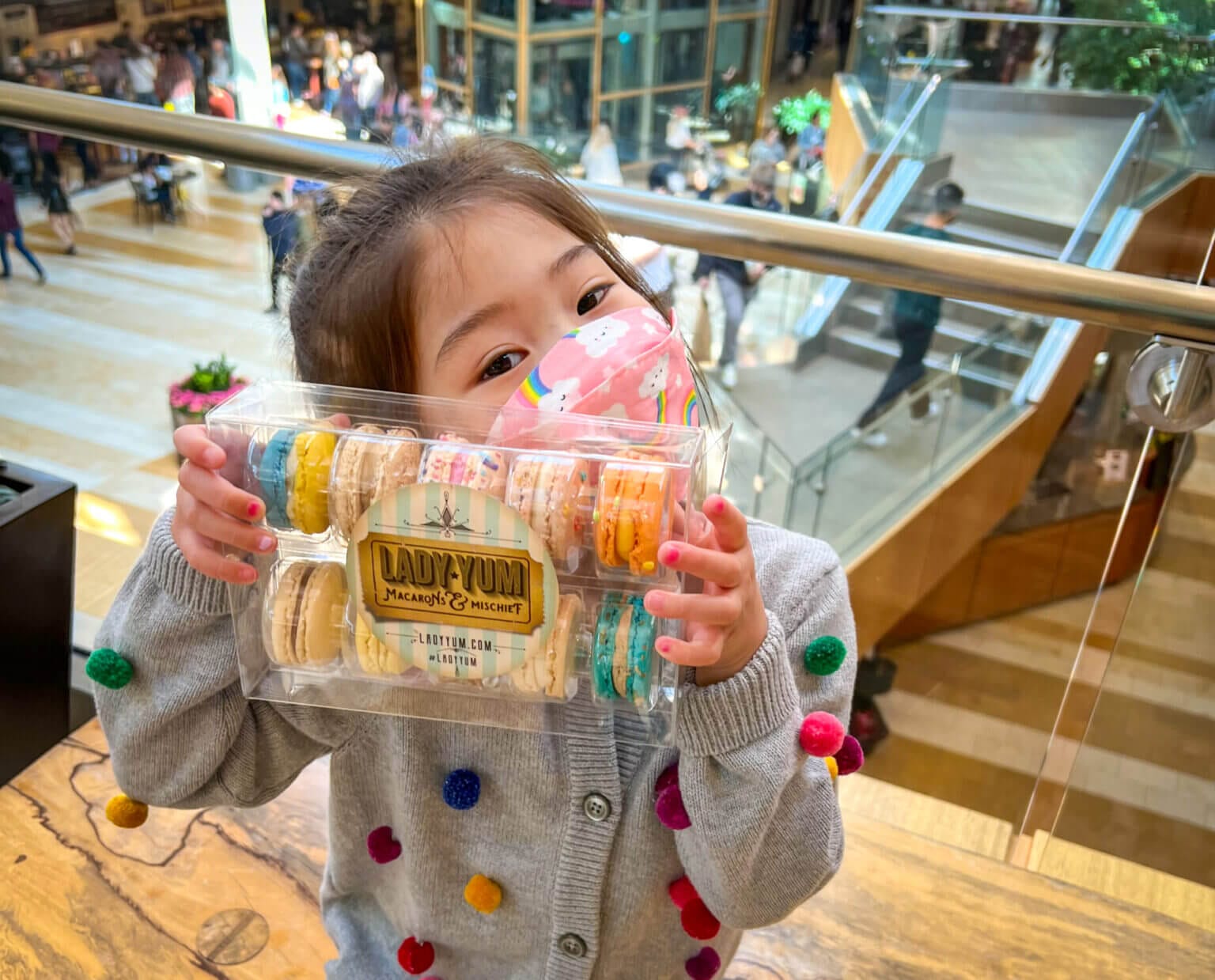 Little girl holding a pack of 12 Lady Yum macarons in Bellevue Collections shopping center