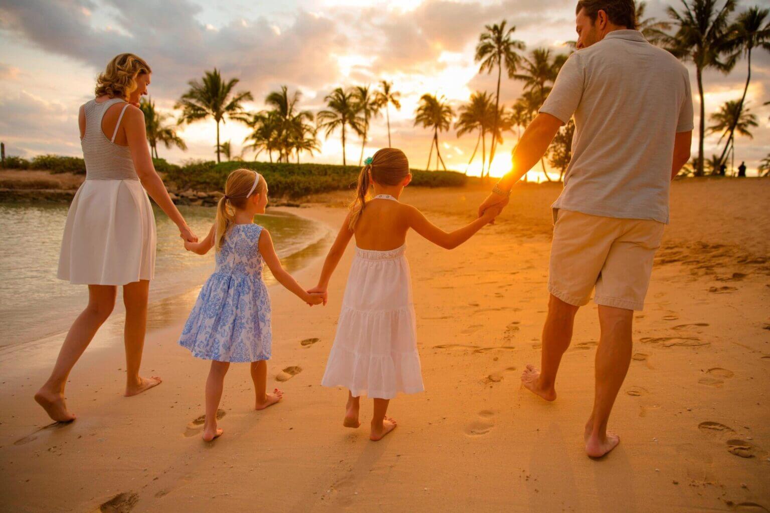 Family with two kids walking on the sandy beach at KoOlina Coves next to Marriott Resort on Oahu, with a sunset in the background. A family-friendly resort.