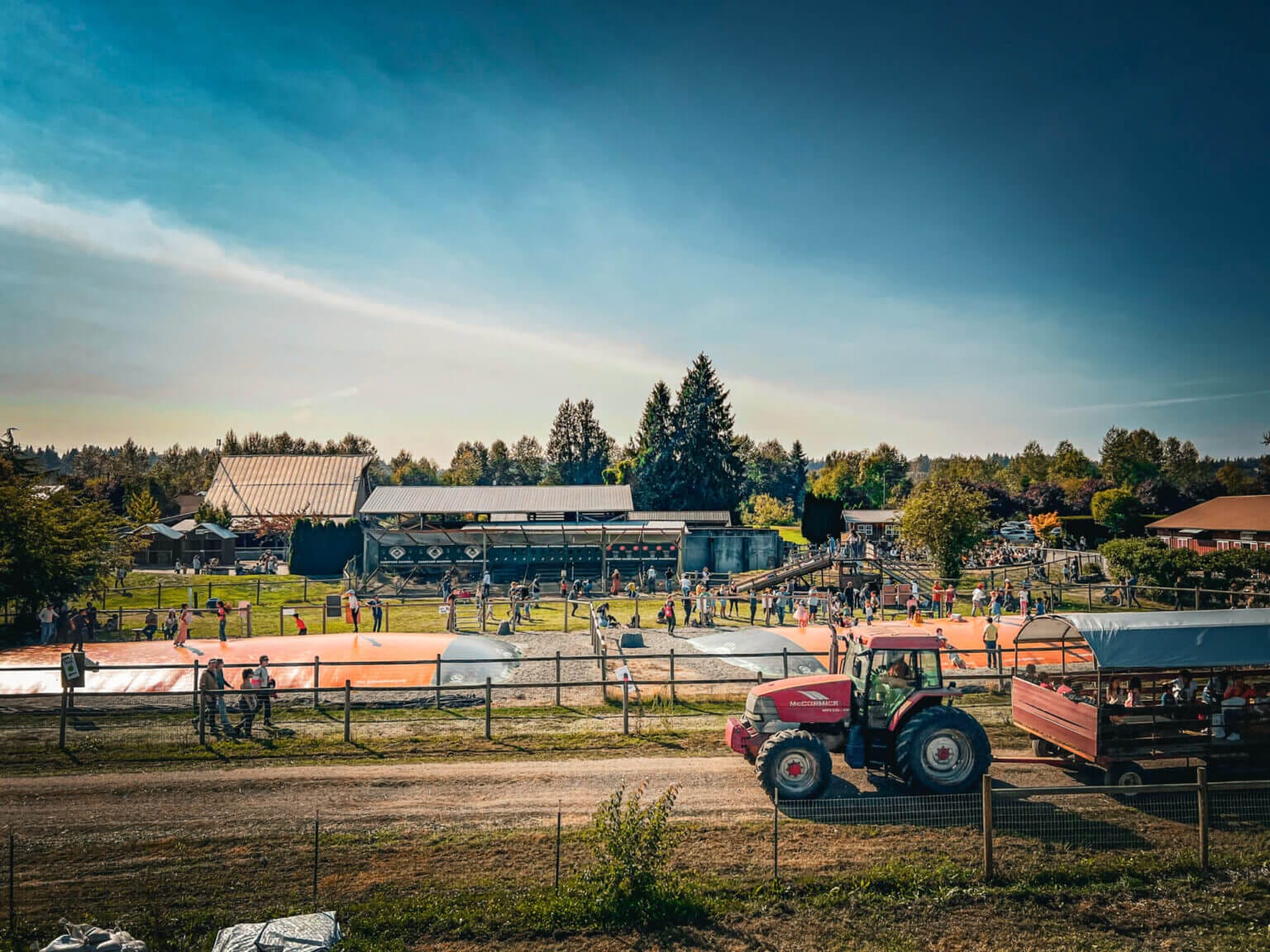 Kids playing at jumping pillows and the play area while a tractor ride passes by at Swans Trail Farm during the fall festival, a fun fall activity with kids.