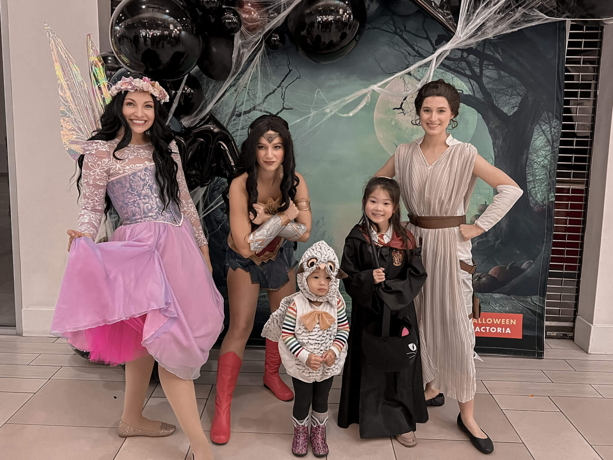 Safe Halloween trick-or-treating at The Marketplace at Factoria in Bellevue for kids, with candy from participating shops and fun photo ops with dressed-up characters and backdrops. Two little sisters take photos with their idols: a princess, Wonder Woman, and Rey from Star Wars