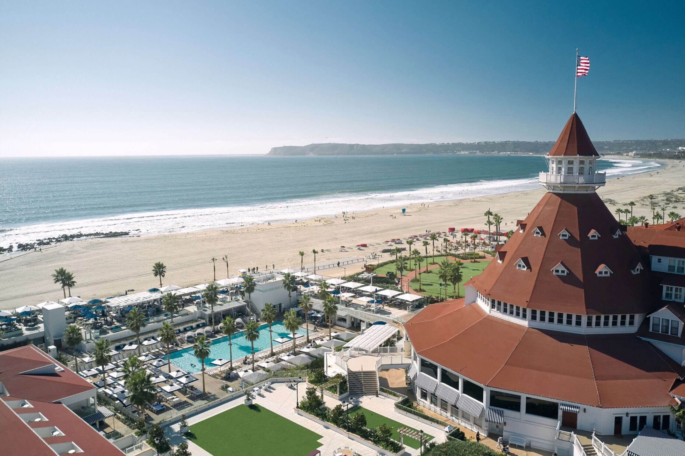 Aerial view of Hotel del Coronado, showcasing its luxurious pool and the famous Coronado Beach in San Diego. A historic and iconic beachfront resort, it’s a popular family vacation destination offering stunning ocean views, family-friendly activities, and world-class amenities.