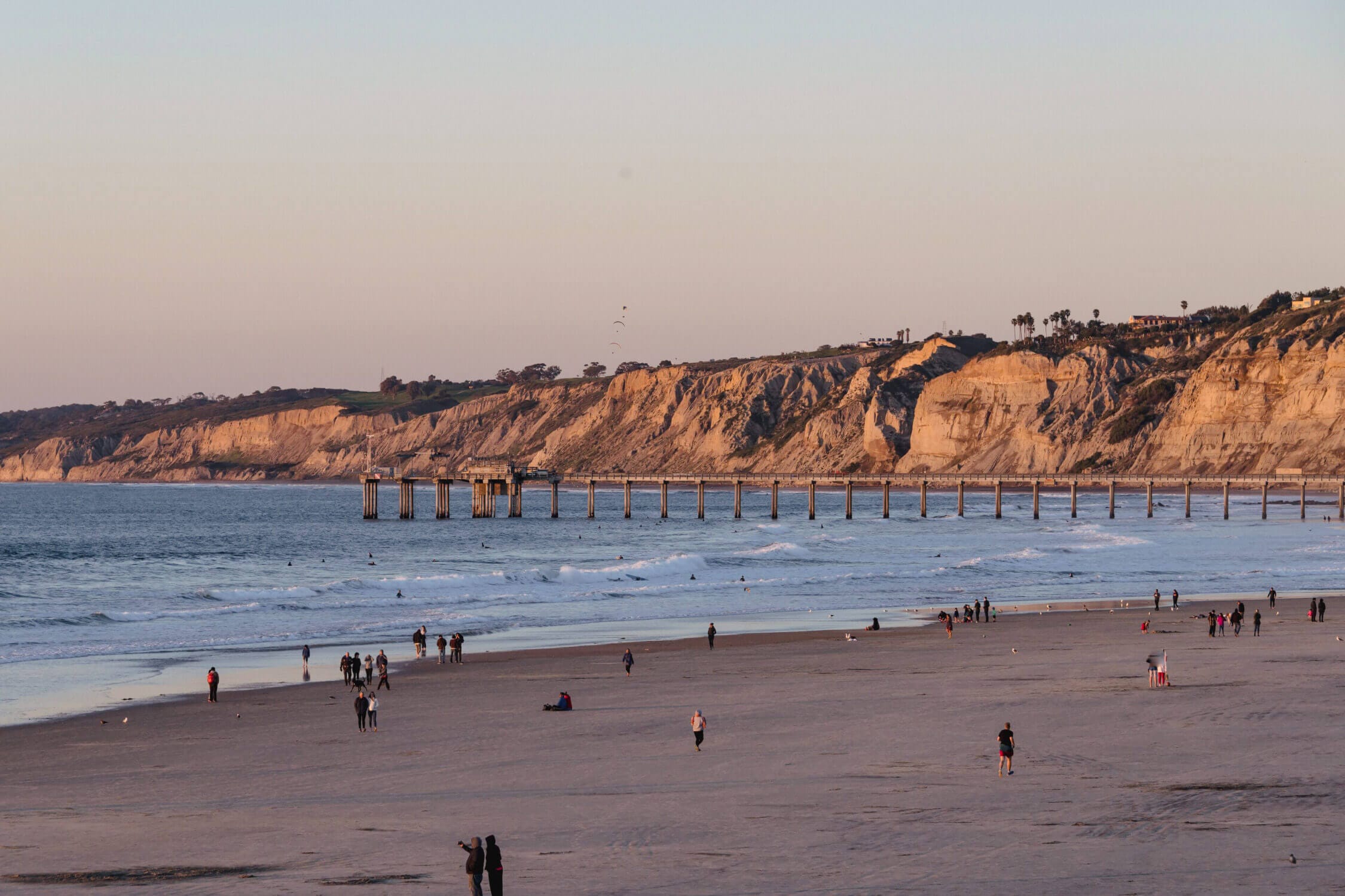 San Diego’s La Jolla Beach and Pier, with people strolling along the sandy shoreline, is a must-visit destination for any family vacation with kids.