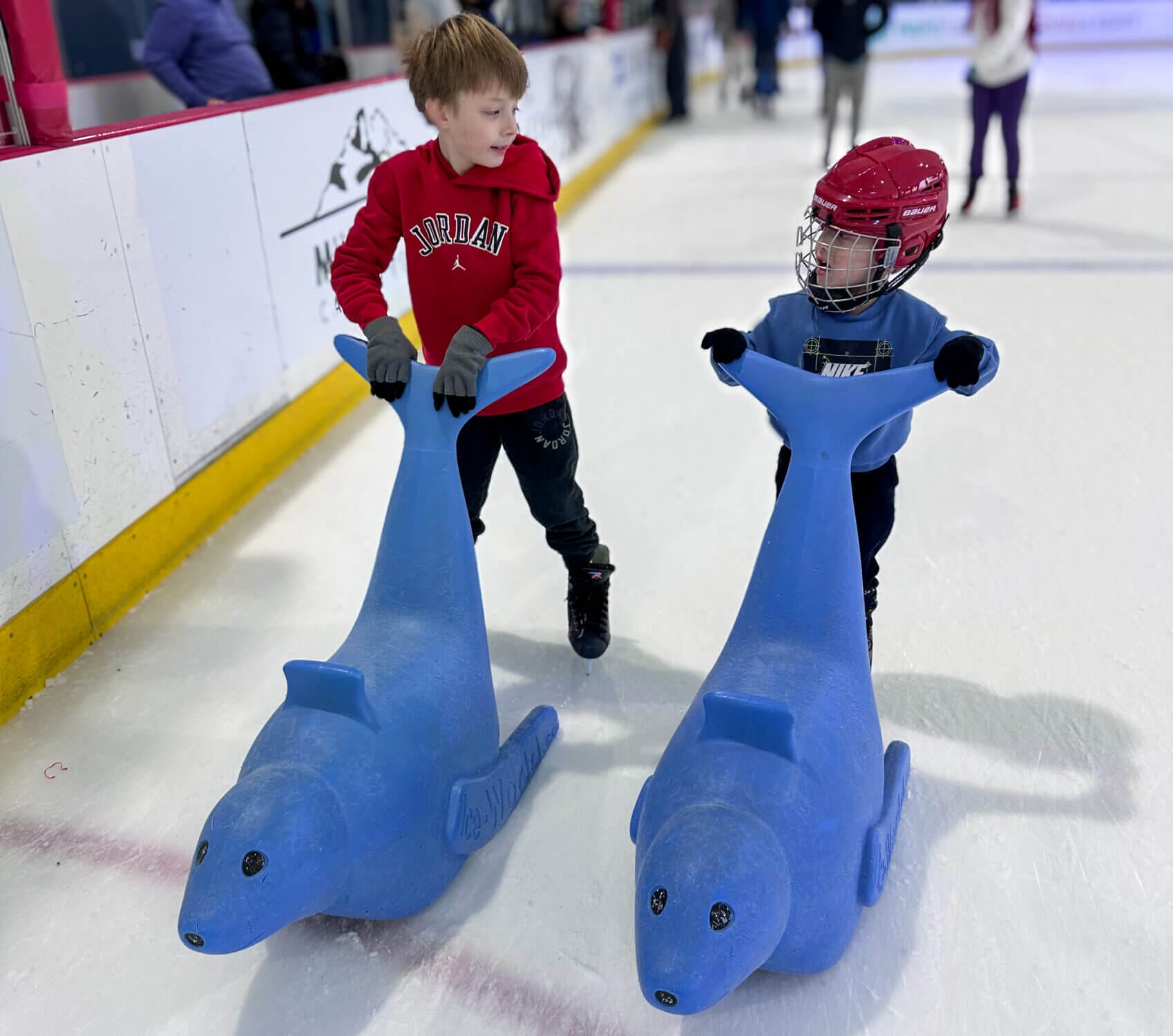 At the Kraken Community Iceplex, families can enjoy public ice skating on the same rink where the Seattle Kraken train. Young kids and beginners can use skating aids like the Seal to help them balance and glide with confidence. Here, two young boys are seen skating while holding onto the Seal, making for a fun and family-friendly experience at this premier hockey facility in Seattle.