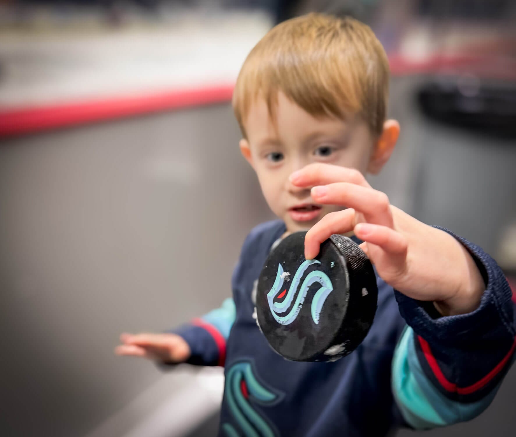 A young boy excitedly holds a wet Seattle Kraken hockey puck, a special keepsake from the team’s practice session. He was lucky enough to have an official practice puck tossed over the plexiglass by one of the players. The Kraken players and coaches love interacting with young fans, often tossing used practice pucks as fun souvenirs. Attending a Seattle Kraken practice at the Kraken Community Iceplex is a fantastic family-friendly experience where kids can get up close to the action, watch their favorite players train, and maybe even take home a piece of the game