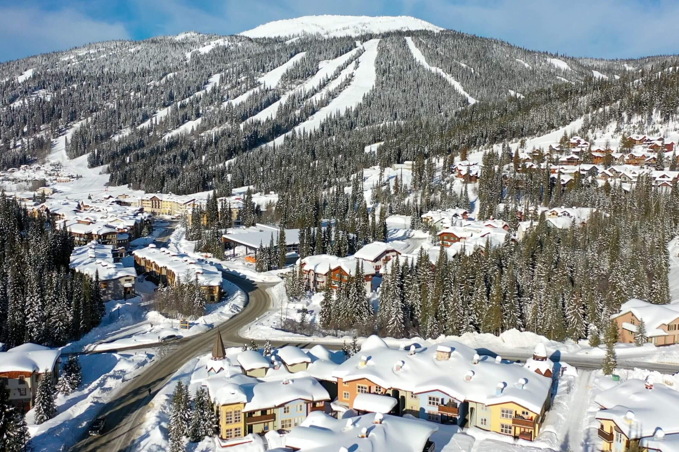 This stunning aerial view of Sun Peaks showcases the charming cluster of townhouses nestled at the base of the mountain, surrounded by pristine snow and a network of ski trails weaving down the slopes. The layout highlights the resort’s ski-in/ski-out convenience, where accommodations are just steps from the action. The snow-covered rooftops and serene alpine backdrop reflect the peaceful, well-designed layout of the village—ideal for families seeking both adventure and comfort. With the towering mountains in the background and direct access to groomed runs, Sun Peaks offers a picture-perfect winter escape that combines cozy lodging with world-class skiing