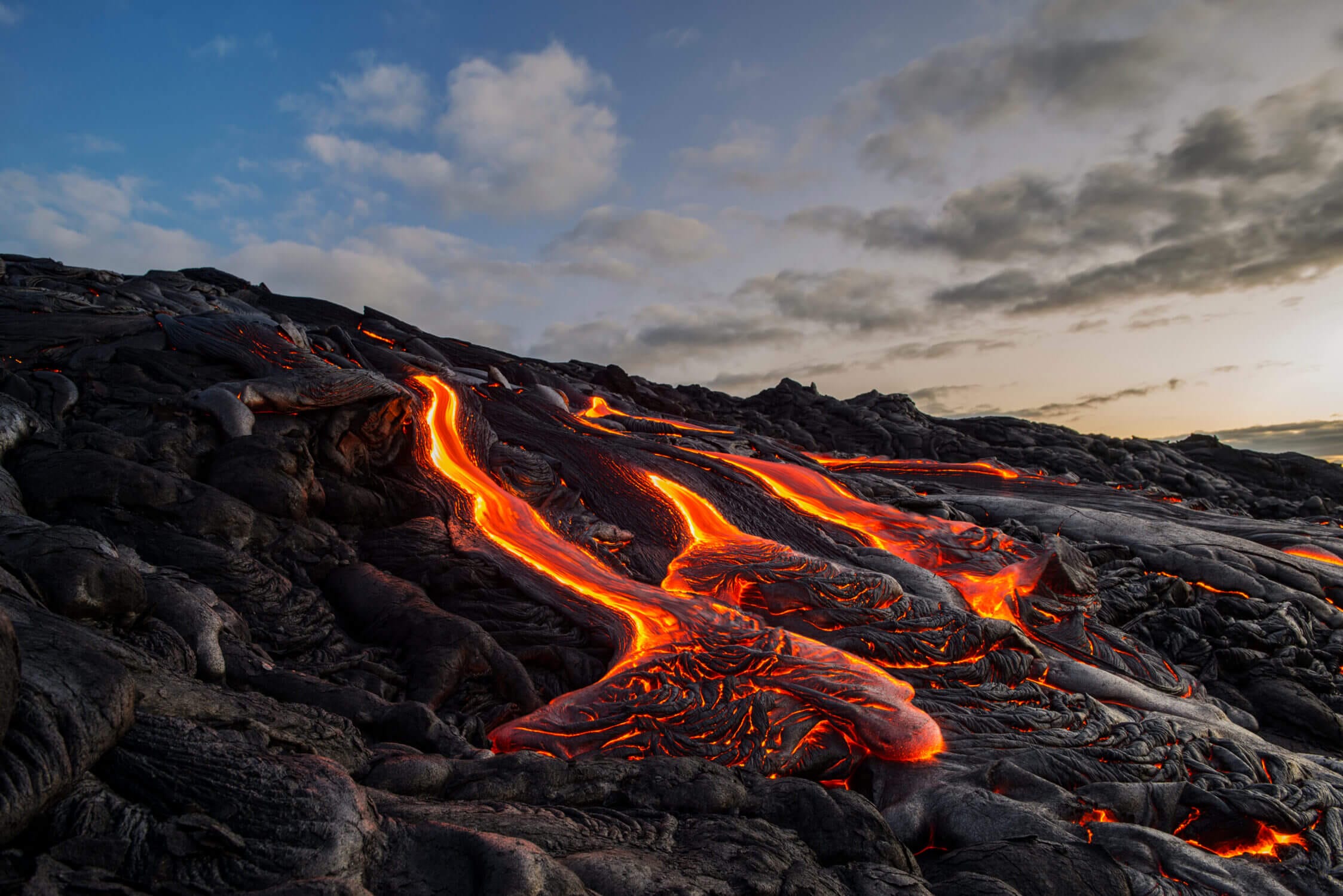 Dramatic view of lava flowing down a hillside on the Big Island of Hawaii, with glowing red molten rock framed by hardened black lava. Featured in our Hilo vs. Kona travel guide, this image highlights the island’s powerful volcanic landscape and serves as a reminder of Hawaiian cultural beliefs—especially the legend of Pele, the volcano goddess. Taking lava rocks home is considered disrespectful and believed to bring bad luck.