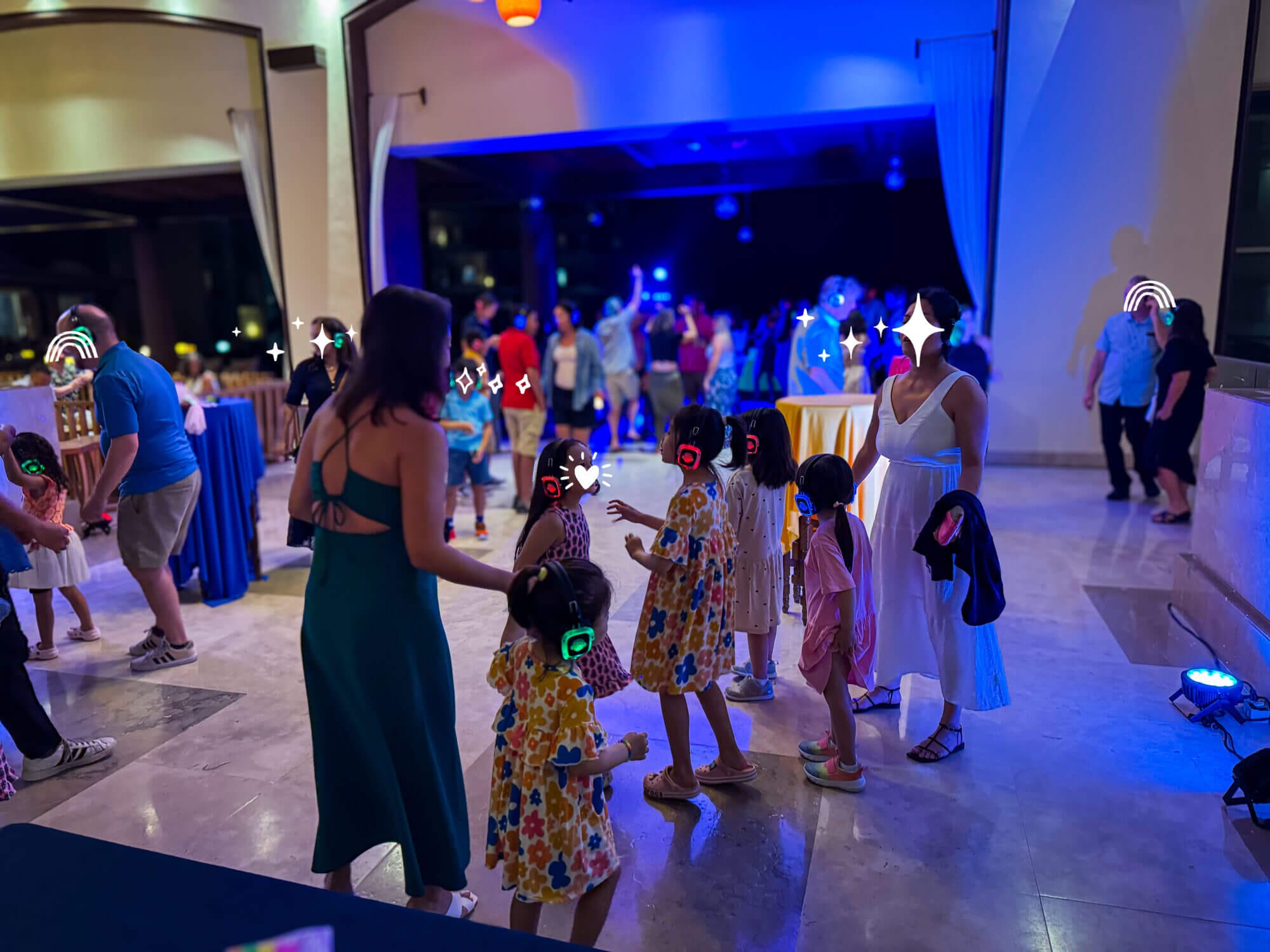 Kids and families enjoy the nighttime silent party in the dimly lit lobby at Dreams Puerto Vallarta, dancing with glowing headphones provided by the resort. This fun, kid-friendly activity is one of many daily events offered, making evenings exciting for both children and parents on their all-inclusive family vacation
