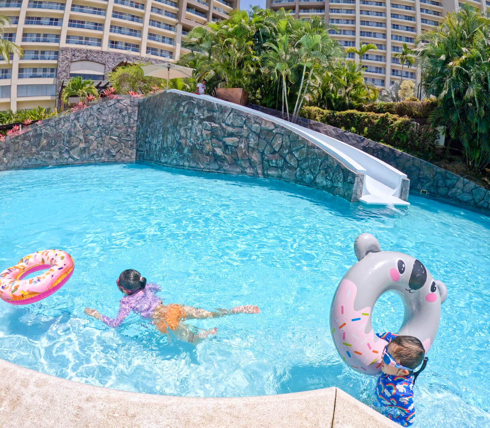 Two young girls swimming with their inflatables at the Dreams Vallarta Bay Resort pool, heading back for another ride down the water slide in the background. Families can bring their own floaties or sometimes find a few available near the pool, adding to the fun. This water slide quickly became a favorite during their spring break getaway, offering endless laughs and excitement. With warm weather, tropical vibes, and kid-friendly features, Dreams Vallarta is the perfect all-inclusive resort for unforgettable family vacations