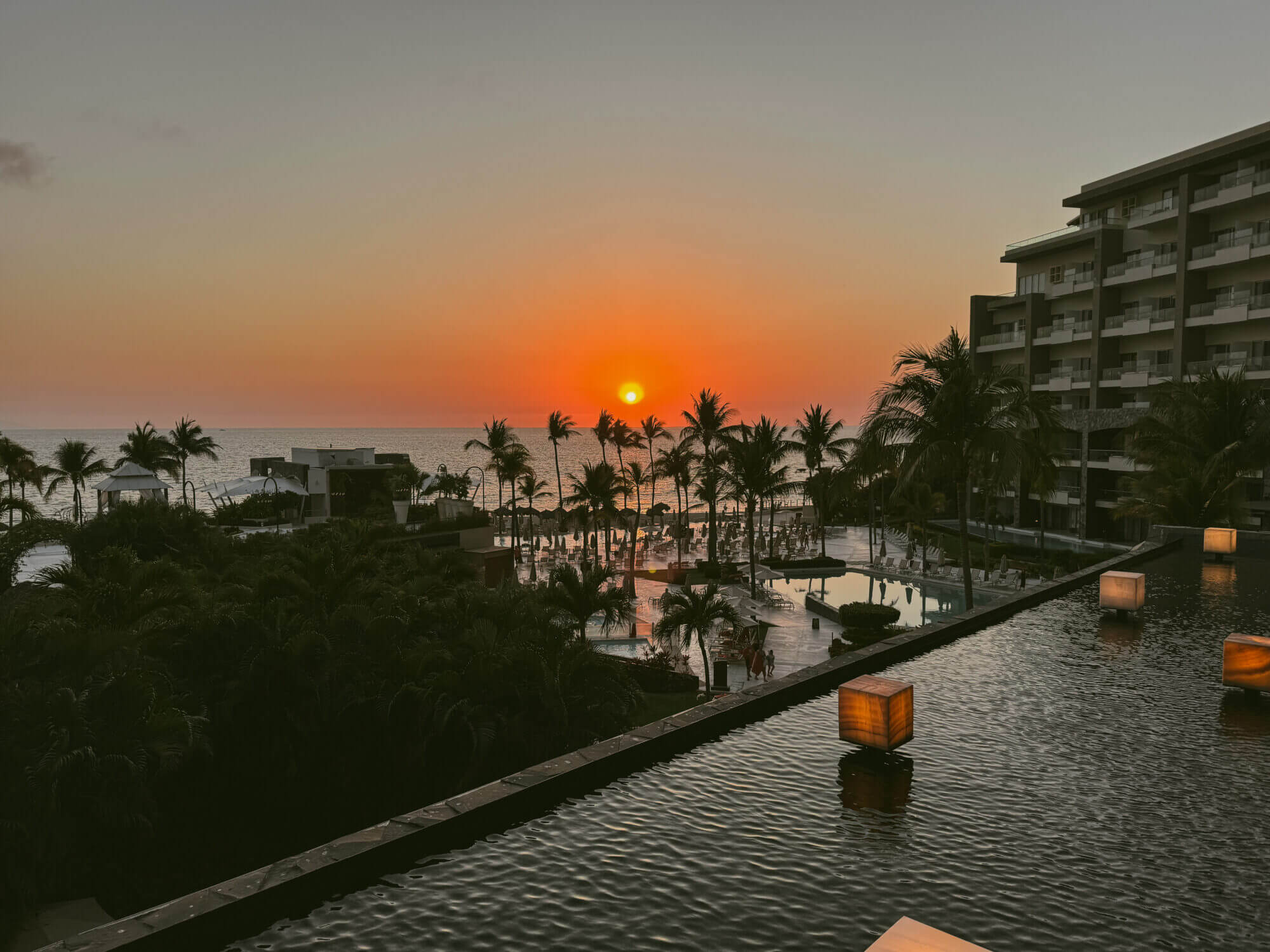 A stunning sunset view from the open-air lobby at Dreams Vallarta Bay Resort, with cozy lounge chairs and a nearby bar creating the perfect atmosphere for a relaxing evening. Parents can unwind with a drink while soaking in the ocean breeze, and just steps away, kids can grab a sweet treat from Coco Café—offering soft-serve ice cream, churros, and other desserts. It’s a magical way to end the day at this all-inclusive, family-friendly resort in Puerto Vallarta.