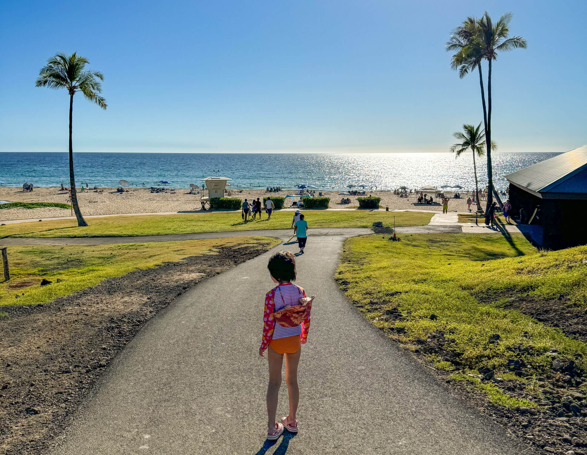 Young girl walking down a sandy pathway toward the stunning white sands and clear blue waters of Hapuna Beach on the Kona side of the Big Island. Widely considered one of the best beaches in Hawaii, Hapuna offers gentle waves, soft sand, and plenty of space for families to relax and play—making it a must-visit destination for those traveling with kids in Kona.