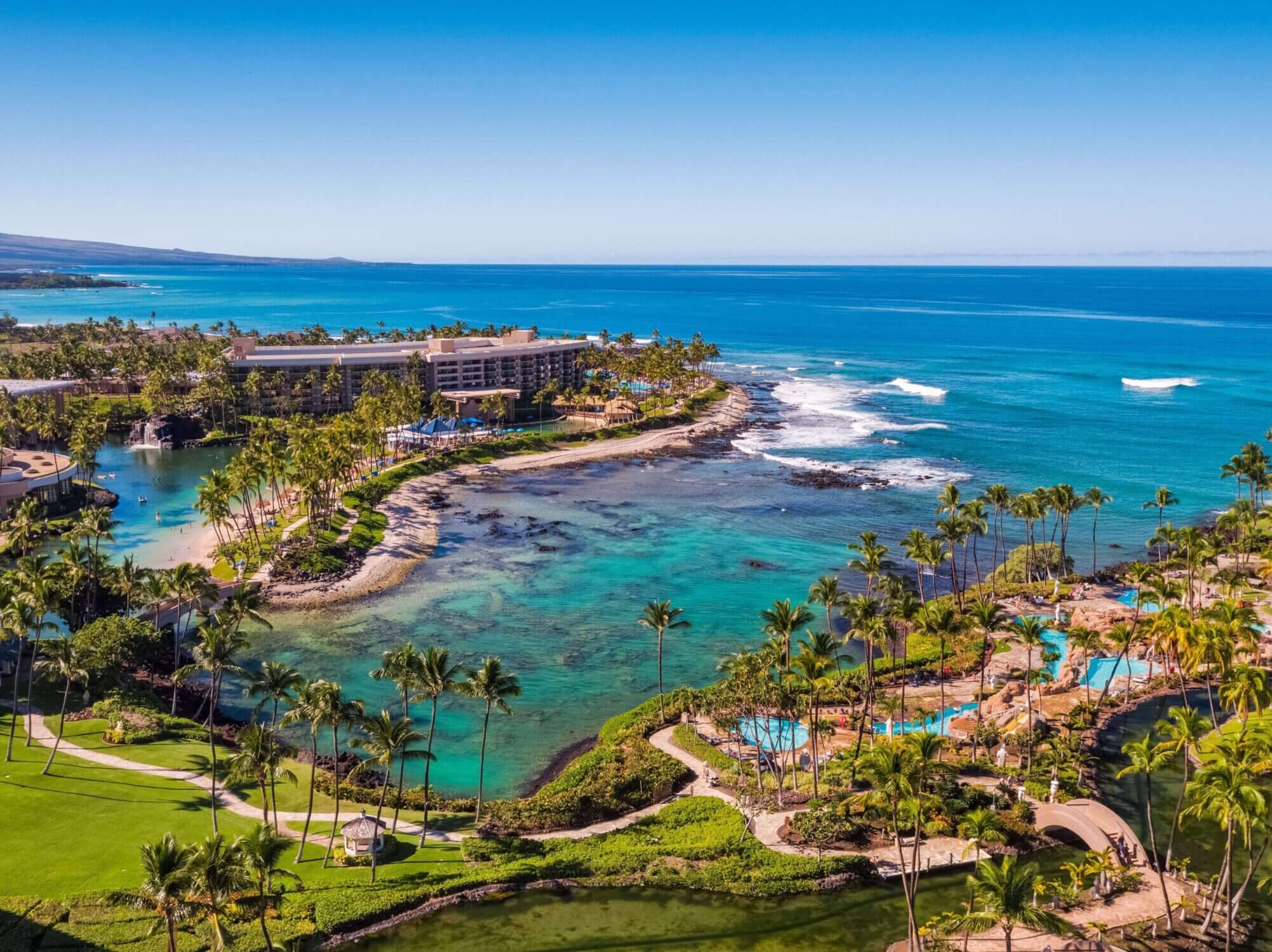 Aerial view of Hilton Waikoloa Village on the Kona coast of the Big Island, showcasing the resort’s sprawling layout with its sparkling swimming pool, saltwater lagoon, and beachfront access to the Pacific Ocean. This luxurious, family-friendly resort is highlighted in our Big Island travel guide for its unique features like the monorail, Dolphin Quest, and scenic walking paths—making it a top pick for families visiting Hawaii.