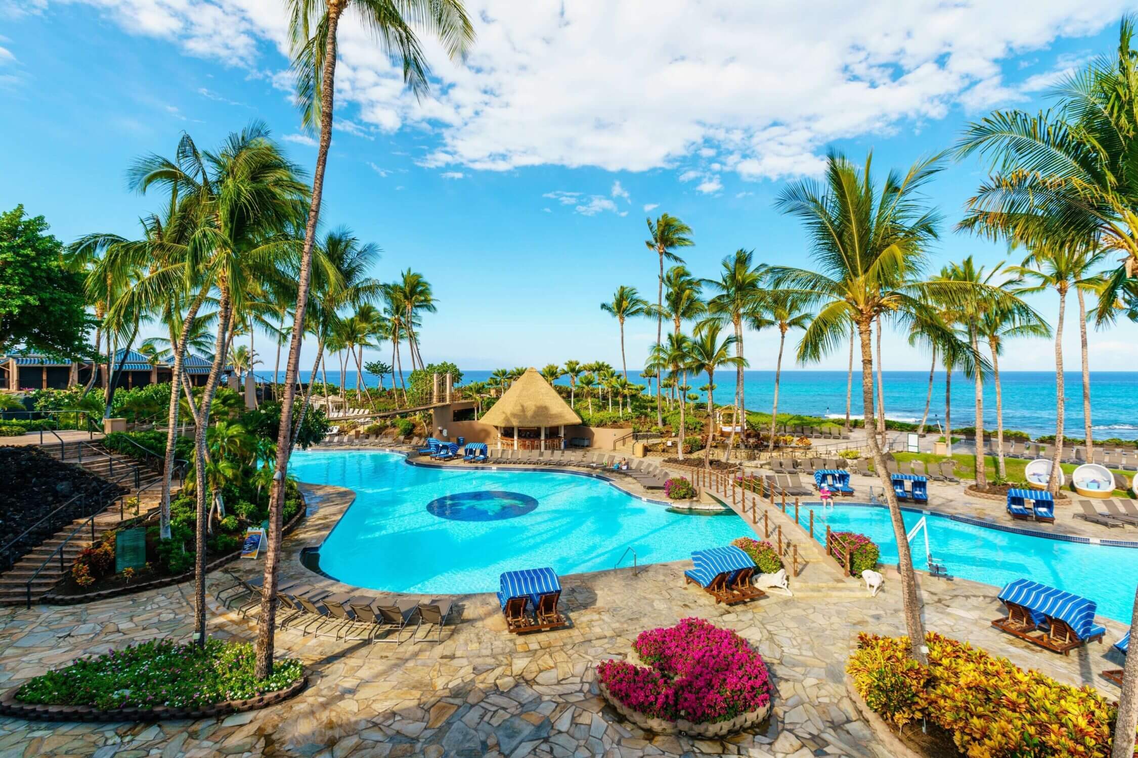 Expansive swimming pool at Hilton Waikoloa Village on the Kona side of the Big Island, surrounded by palm trees and lounge chairs. Featured in our family travel guide, this resort is one of our top picks for families visiting Hawaii, offering kid-friendly amenities, scenic ocean views, and plenty of space for fun and relaxation.