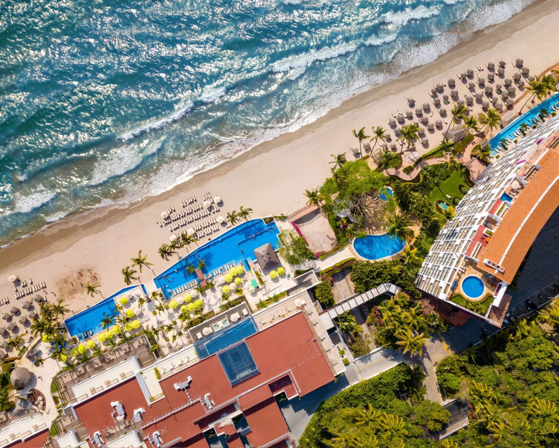 Aerial view of Hyatt Ziva Puerto Vallarta, an all-inclusive beachfront resort nestled between lush green hills and the Pacific Ocean. This family-friendly destination features multiple pools, kid-friendly activities, and private beaches, making it one of our top picks for vacations with kids in Mexico.