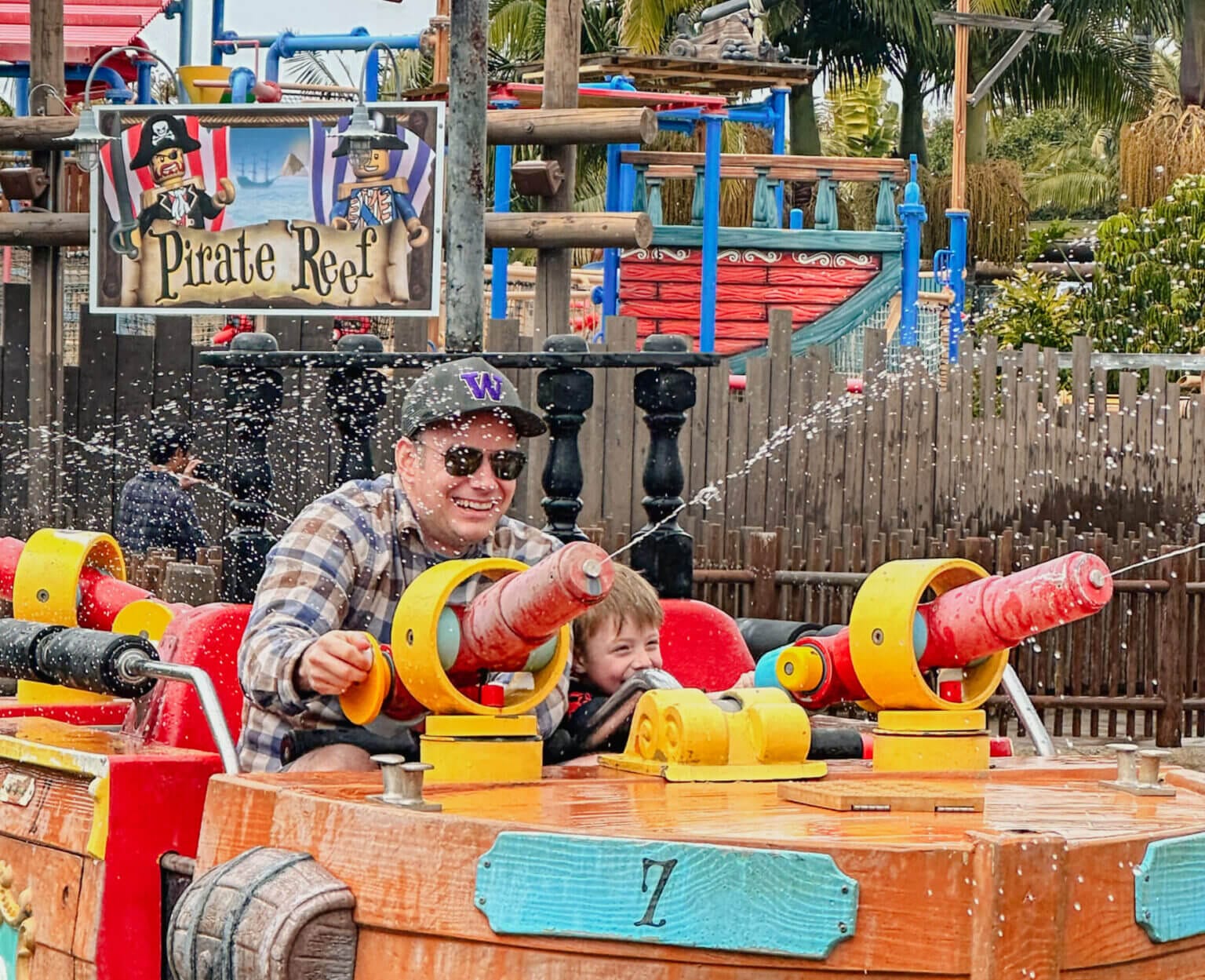 Dad and son team up to shoot water guns at targets on the interactive Pirate Reef ride at LEGOLAND California. This splash-filled attraction lets guests battle it out with water cannons from both the ride and the viewing area, making it a thrilling and fun experience for families visiting with kids.