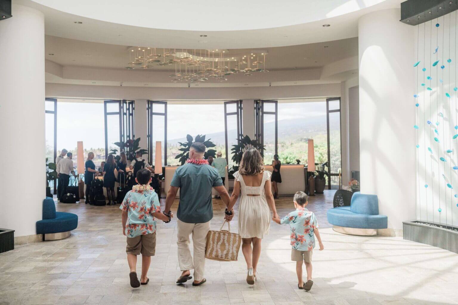 Mom, dad, and two young boys walking hand in hand through the open-air lobby at the Outrigger Kona Resort on the Big Island of Hawaii. This welcoming and spacious resort is ideal for families, offering cultural programs, oceanfront views, and a kid-friendly pool with a waterslide—making it a perfect home base for an unforgettable Hawaii family vacation