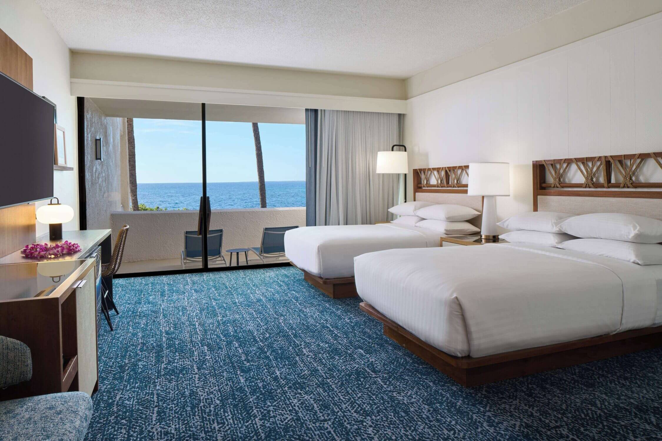 Interior of a two double bed room at the Outrigger Kona Resort on the Big Island of Hawaii, featuring clean and spacious accommodations with island-inspired décor, private lanai, and ocean or garden views. Ideal for families, these rooms offer comfort, space, and convenient access to the resort’s kid-friendly amenities like the waterslide pool and cultural activities.