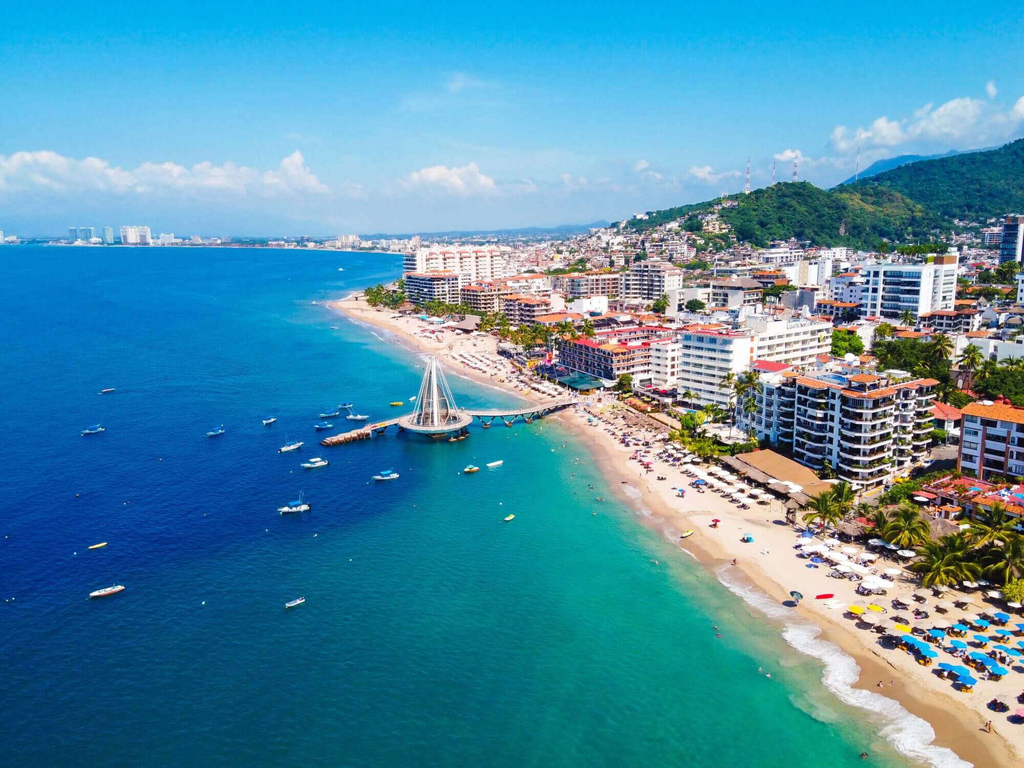 Aerial view of the Puerto Vallarta waterfront featuring the iconic Malecón Boardwalk and the popular Los Muertos Beach Pier. This scenic stretch offers stunning ocean views, public art, vibrant culture, and family-friendly activities—making it a must-visit destination for visitors with kids.
