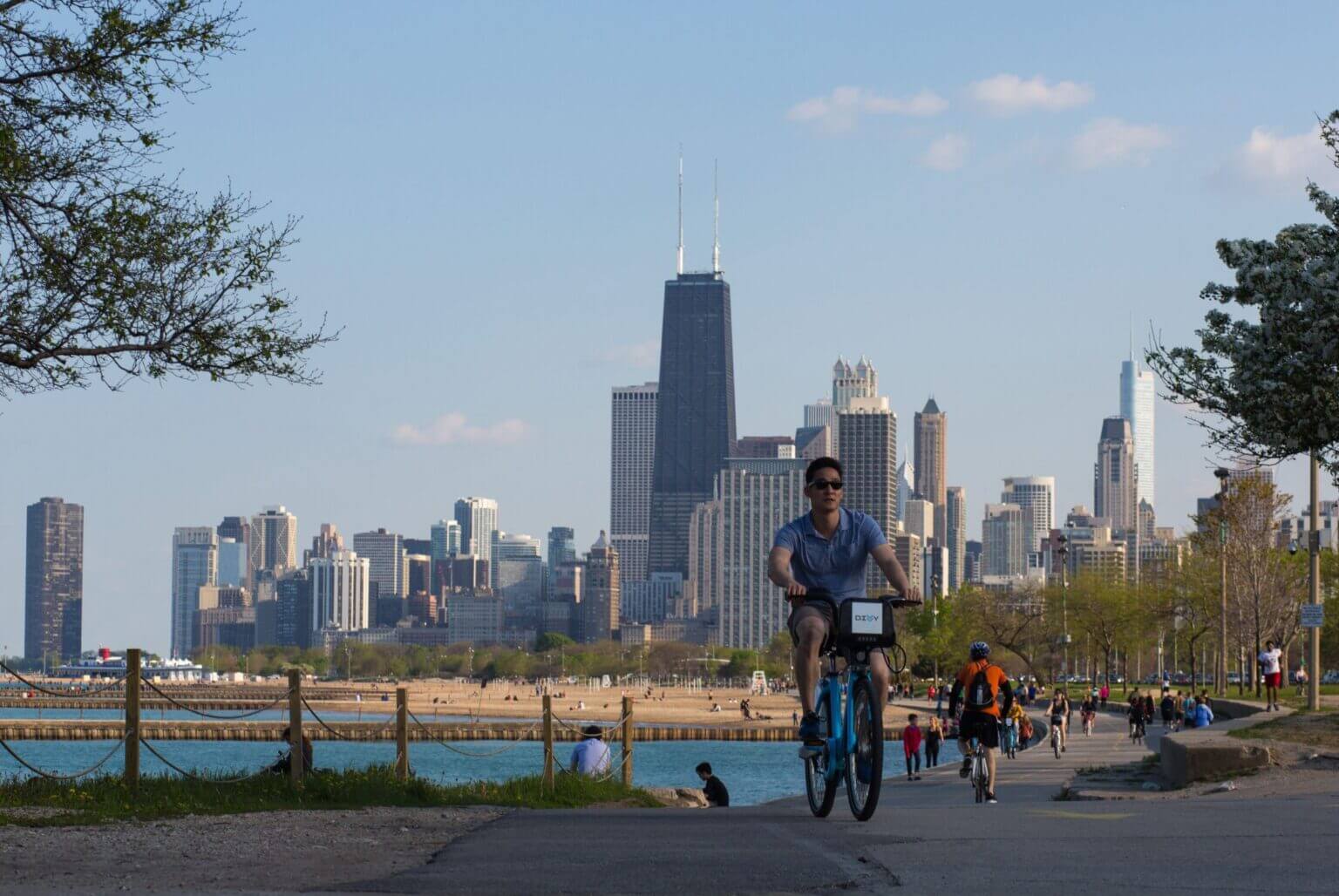 People biking along the scenic trail at Lincoln Park in Chicago, with lush greenery and the Chicago downtown skyline in the background. A perfect kid-friendly outdoor activity offering stunning views and space to roam.