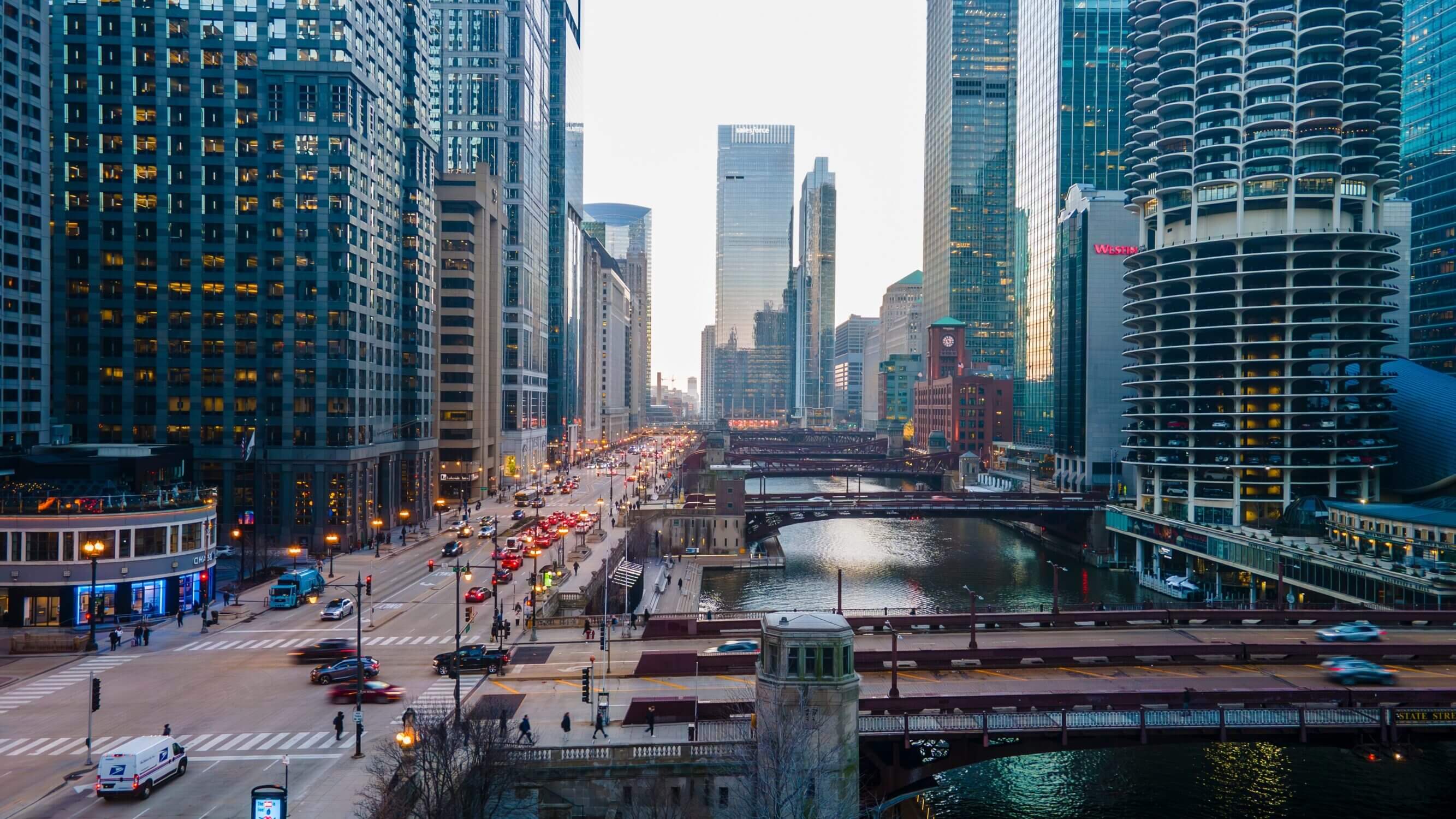 Aerial view of downtown Chicago during an overcast sunset, showcasing the iconic Chicago River winding through the city with multiple bridges and famous skyscrapers nearby, all close to kid-friendly attractions.