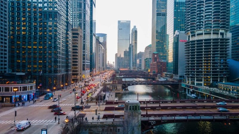 Aerial view of downtown Chicago during an overcast sunset, showcasing the iconic Chicago River winding through the city with multiple bridges and famous skyscrapers nearby, all close to kid-friendly attractions.