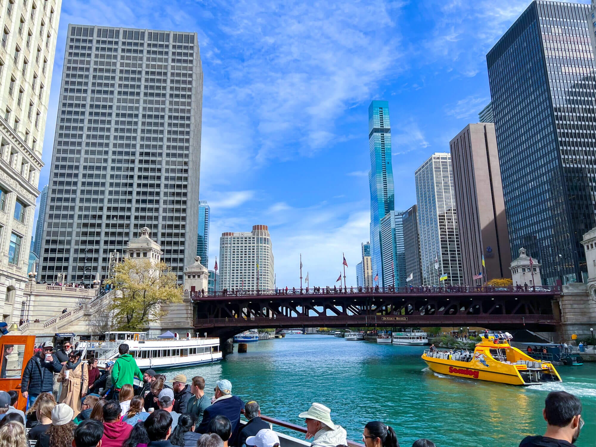 Passengers boarding an architecture boat tour in Chicago, with iconic skyscrapers and historic bridges in the background. A must-do activity for families, offering kids and adults a fun way to learn about the city’s famous buildings while cruising the river.