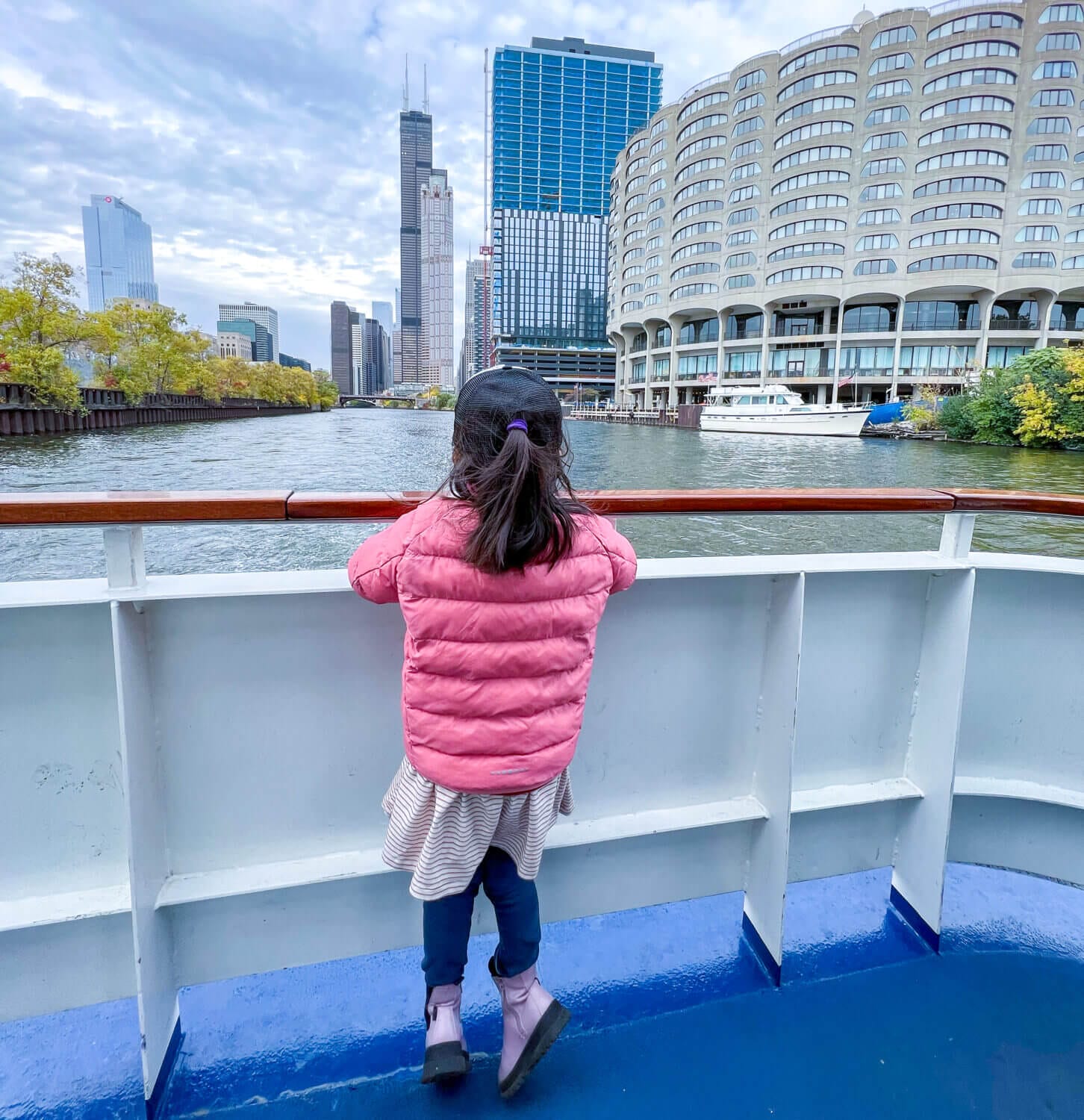 Toddler girl on the back of a Chicago architecture boat tour, gazing out at the river and towering buildings on a sunny day. A memorable family-friendly activity featured in our blog about things to do with kids in Chicago.