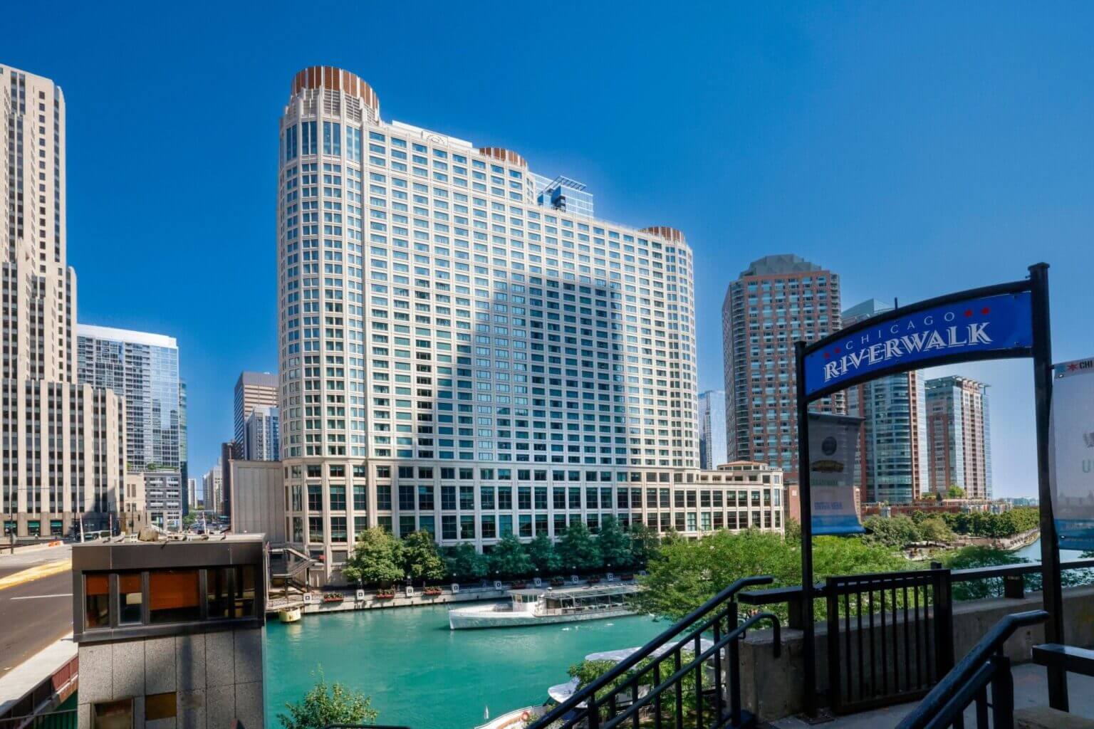 Chicago Riverwalk entry sign with the Sheraton Grand Chicago in the background on a sunny day; one of the top family-friendly things to do in Chicago with kids, offering beautiful waterfront views, walking paths, and easy access to restaurants and attractions.