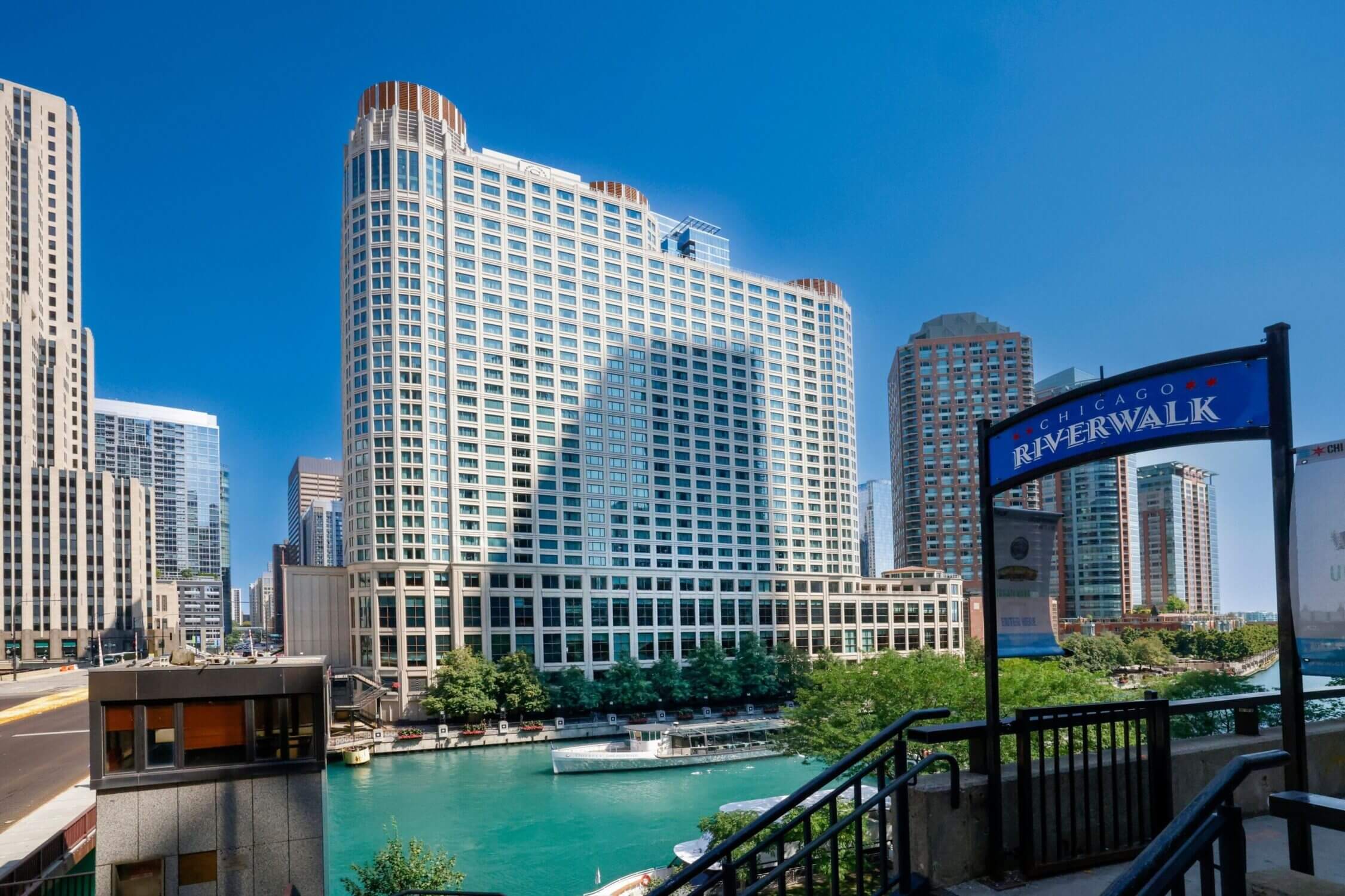 Chicago Riverwalk entry sign with the Sheraton Grand Chicago in the background on a sunny day; one of the top family-friendly things to do in Chicago with kids, offering beautiful waterfront views, walking paths, and easy access to restaurants and attractions.