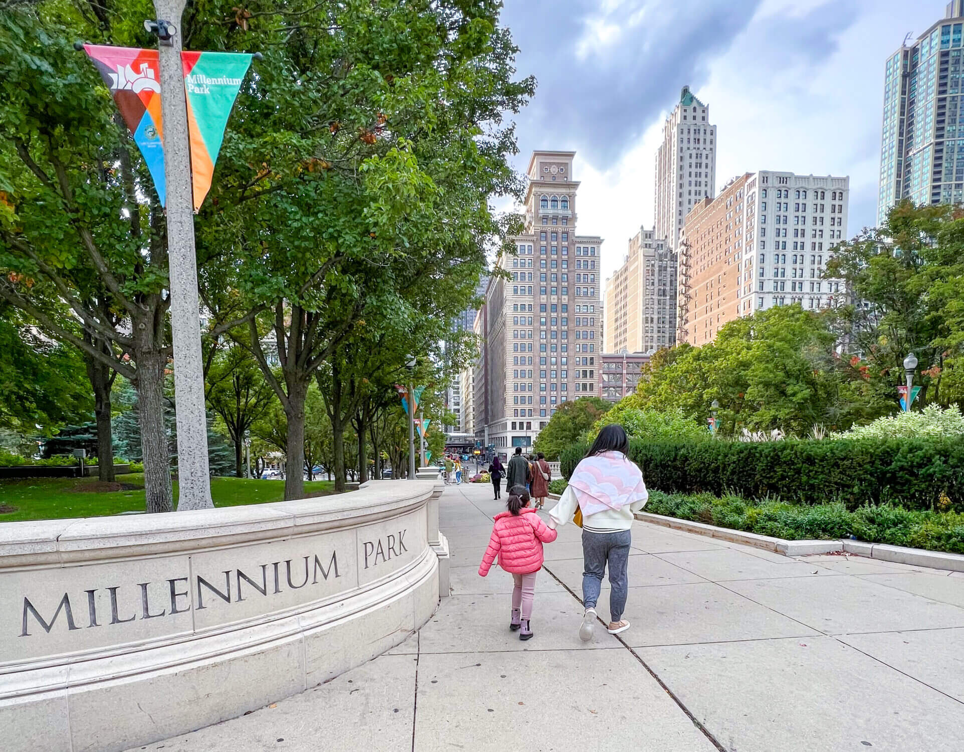 Mom and daughter walking hand in hand through Chicago’s Millennium Park, with iconic skyscrapers and architectural landmarks in the background—highlighting one of the top family-friendly spots to explore in the city.