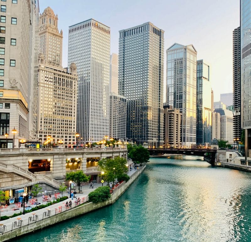 A scenic view of the River North neighborhood in Chicago, featuring the iconic Chicago Riverwalk with towering high-rises and renowned architecture lining the water—showcasing the city’s urban beauty and walkability.