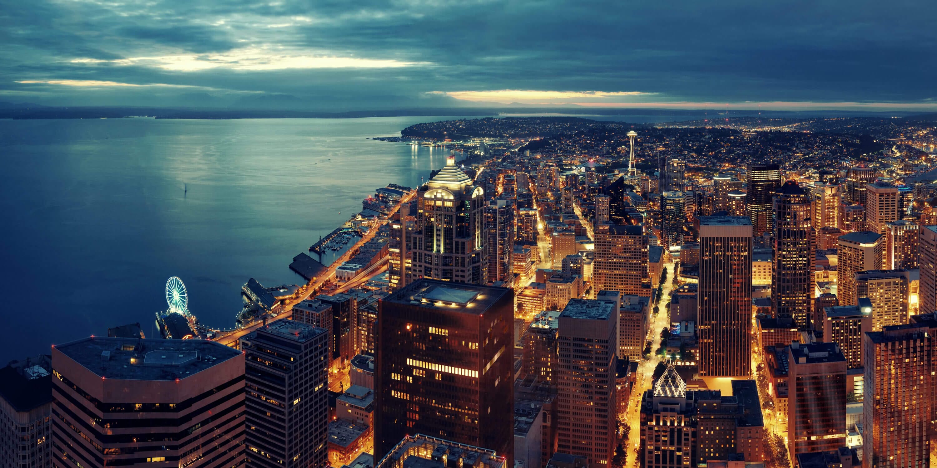 Aerial view of downtown Seattle at night, beautifully lit with the iconic Space Needle and Seattle Great Wheel glowing in the background—highlighting the vibrant atmosphere near many of the best family-friendly hotels in downtown Seattle.