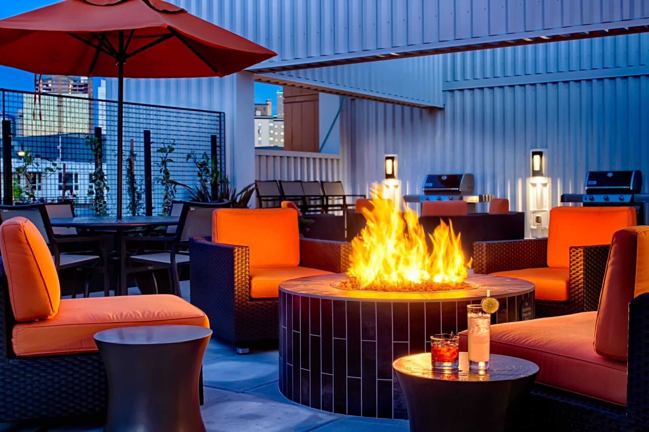 Rooftop deck at Hyatt House Queen Anne in Seattle, featuring cozy fireplace seating, barbecue grills, and panoramic views of the Space Needle and city skyline—perfect for families to relax after a day of exploring.