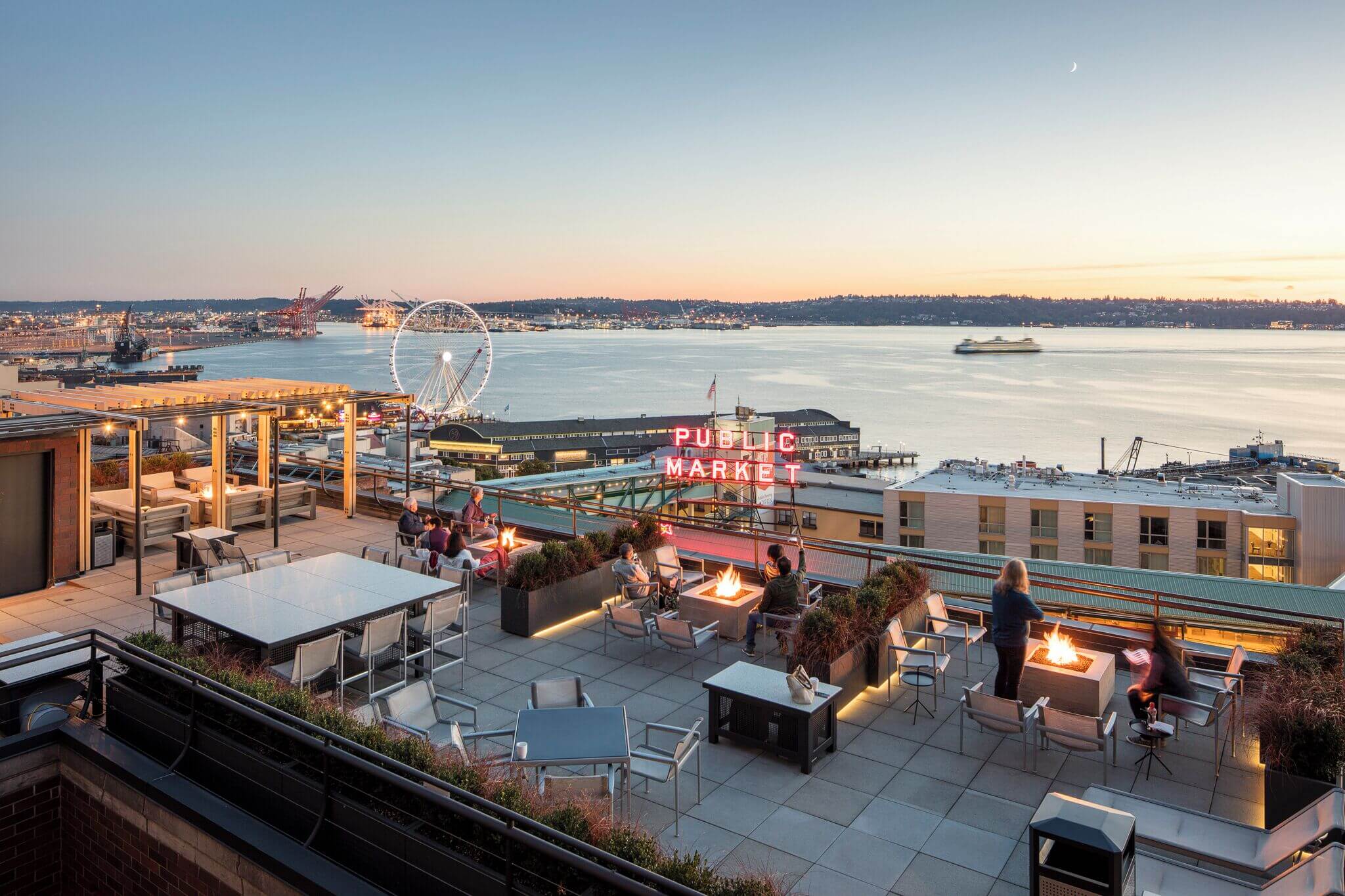Rooftop balcony view from Inn at the Market, overlooking the iconic Pike Place Market neon sign, Seattle’s waterfront, and the Ferris wheel in the distance. A relaxing and scenic spot, perfect for families staying in downtown Seattle.